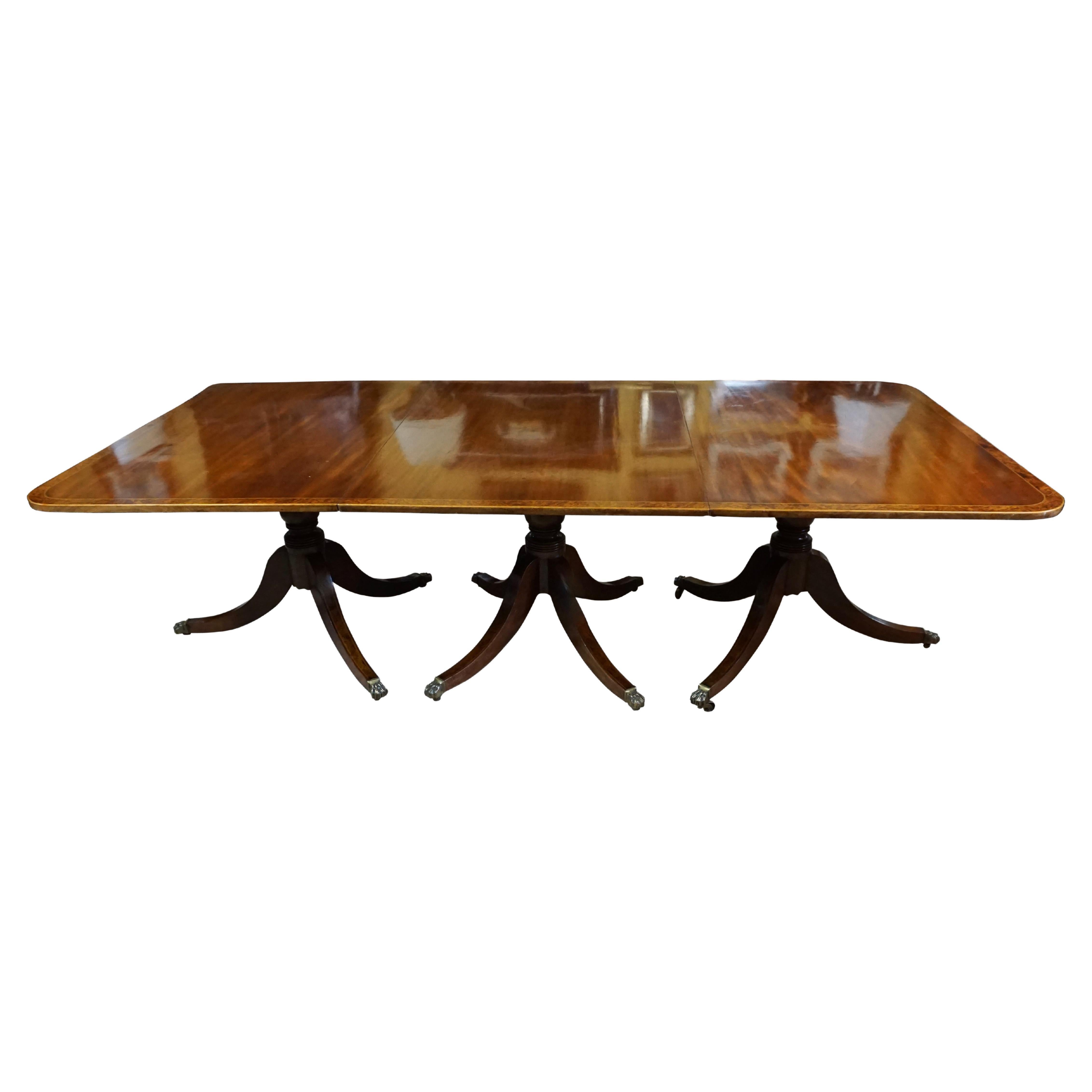 A good quality English inlaid mahogany Georgian style three pedestal dining table retaining its 2 original leafs, the top with elegant burl elm crossbanding finished with boxwood trim and supported on 3 well-turned pedestals with burl elm inlaid