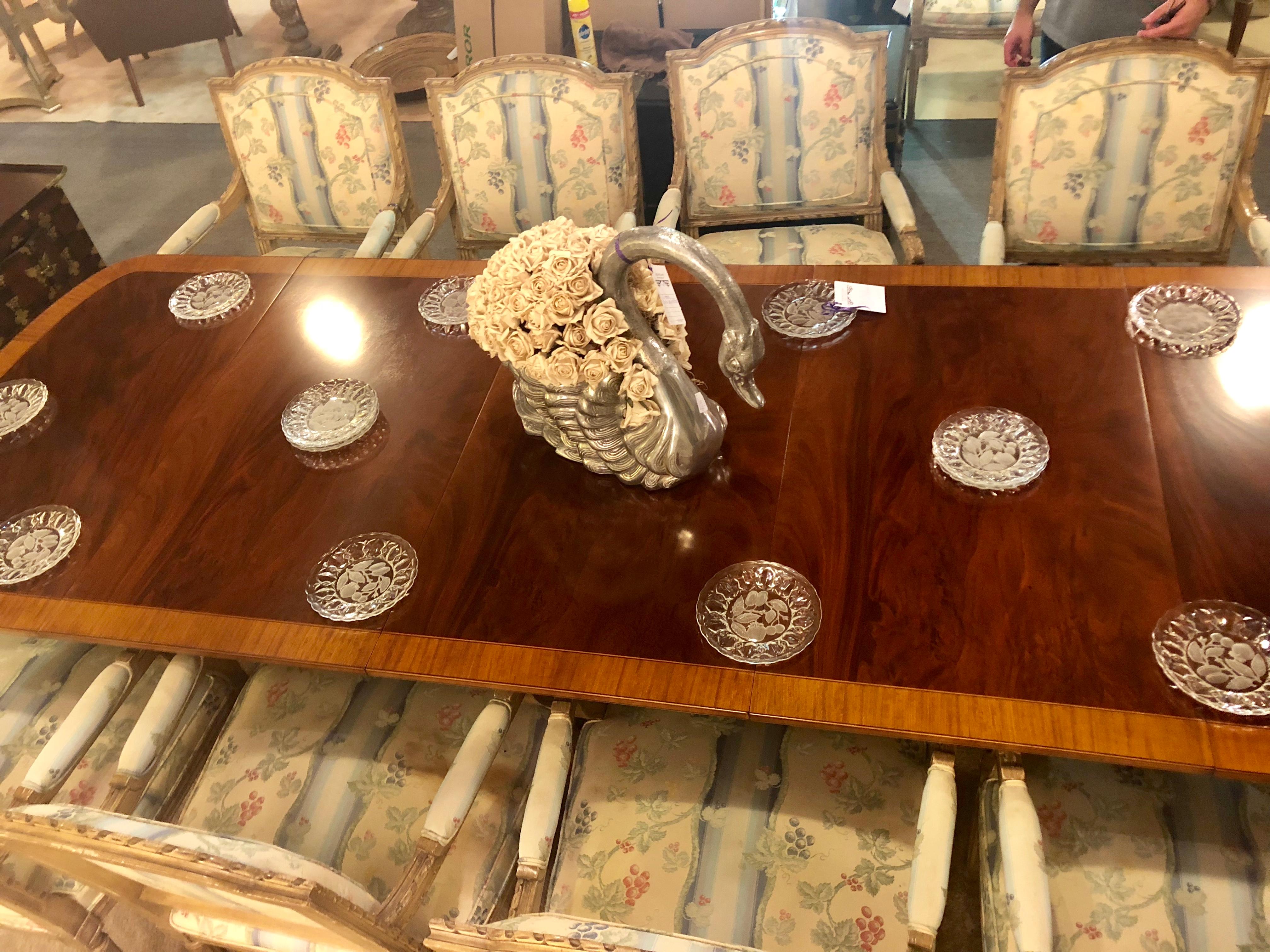 A fully refinished crotch mahogany satin wood banded triple pedestal Regency style dining table having four leaves. This simply stunning and multi versatile dining table is six feet in length and fully extends to multiple sizes having two 24 inch