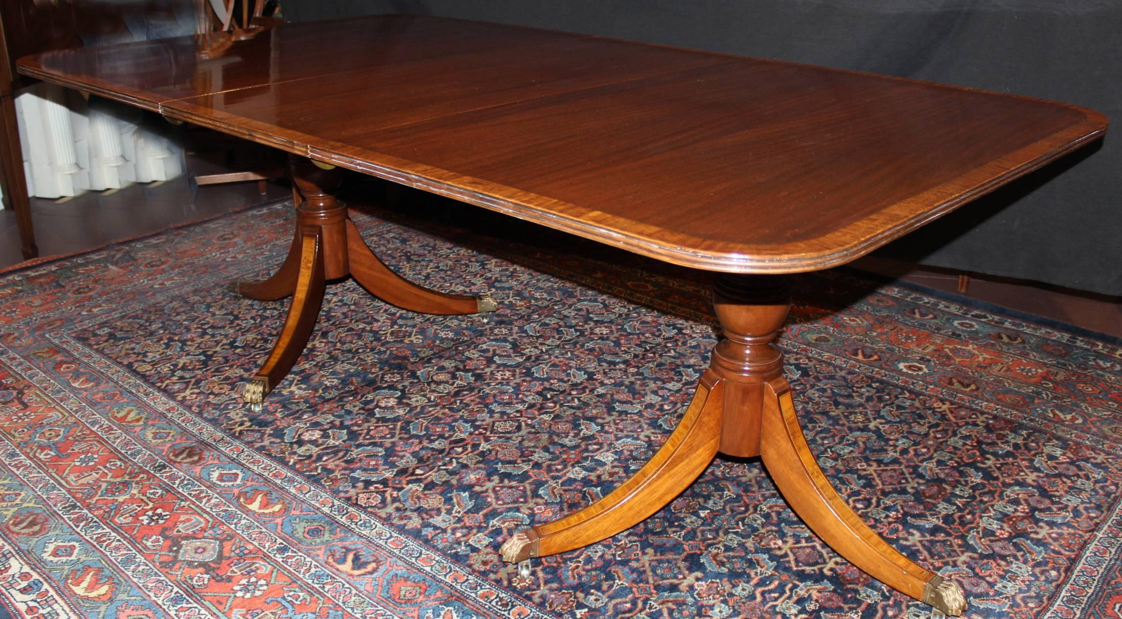 A fine Georgian style rectangle mahogany veneered double pedestal dining table, its top with rounded corners, triple reeded edge, satinwood inlaid border, each turned pedestal with three down swept legs also highlighted with satinwood inlay,