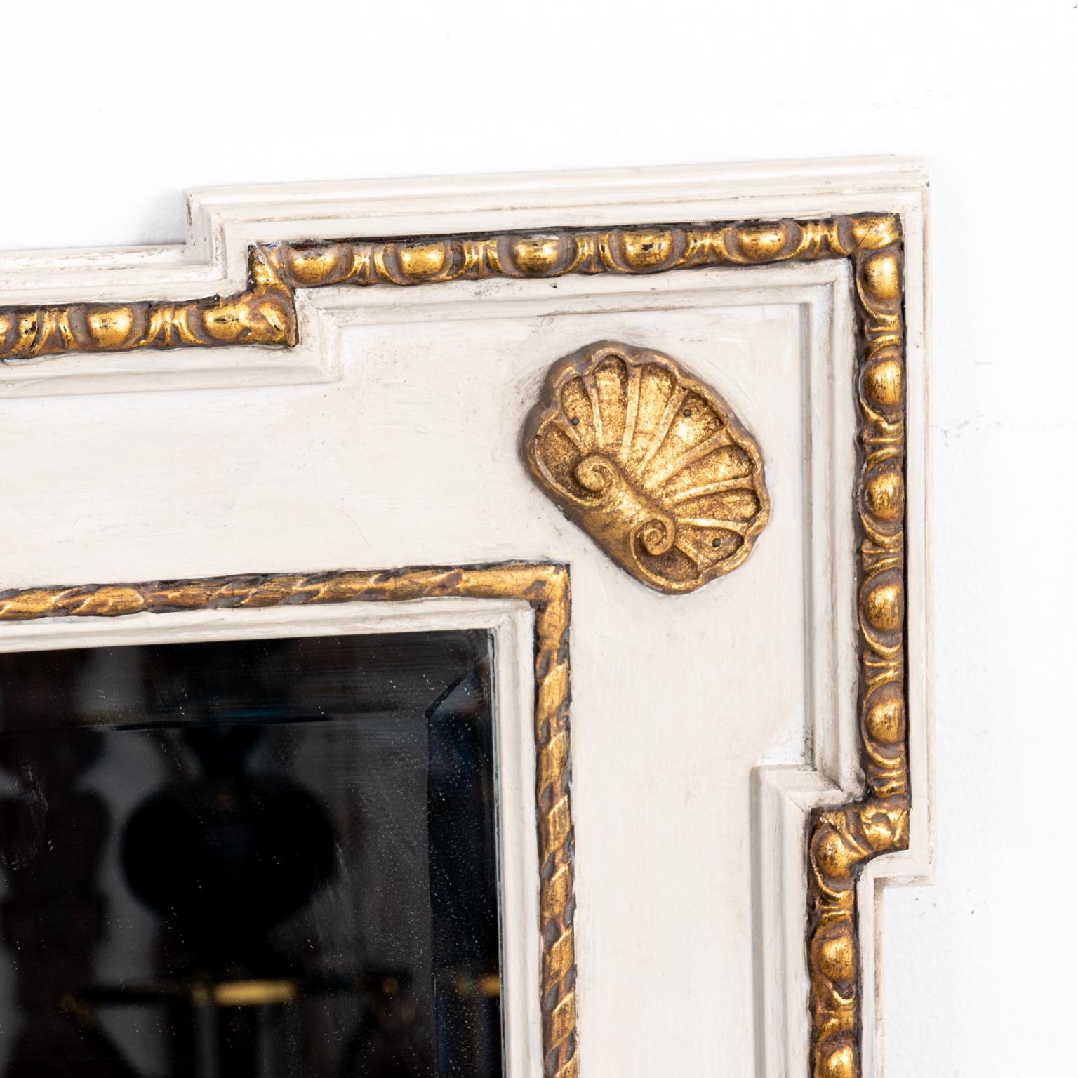 Circa 1940s architectural painted and gilt Georgian style mirror with egg-and-dart molding surrounding the exterior perimeter of the mirror frame. Each dog ear corner features a gilded scallop seashell motif with the inner molding accented by a