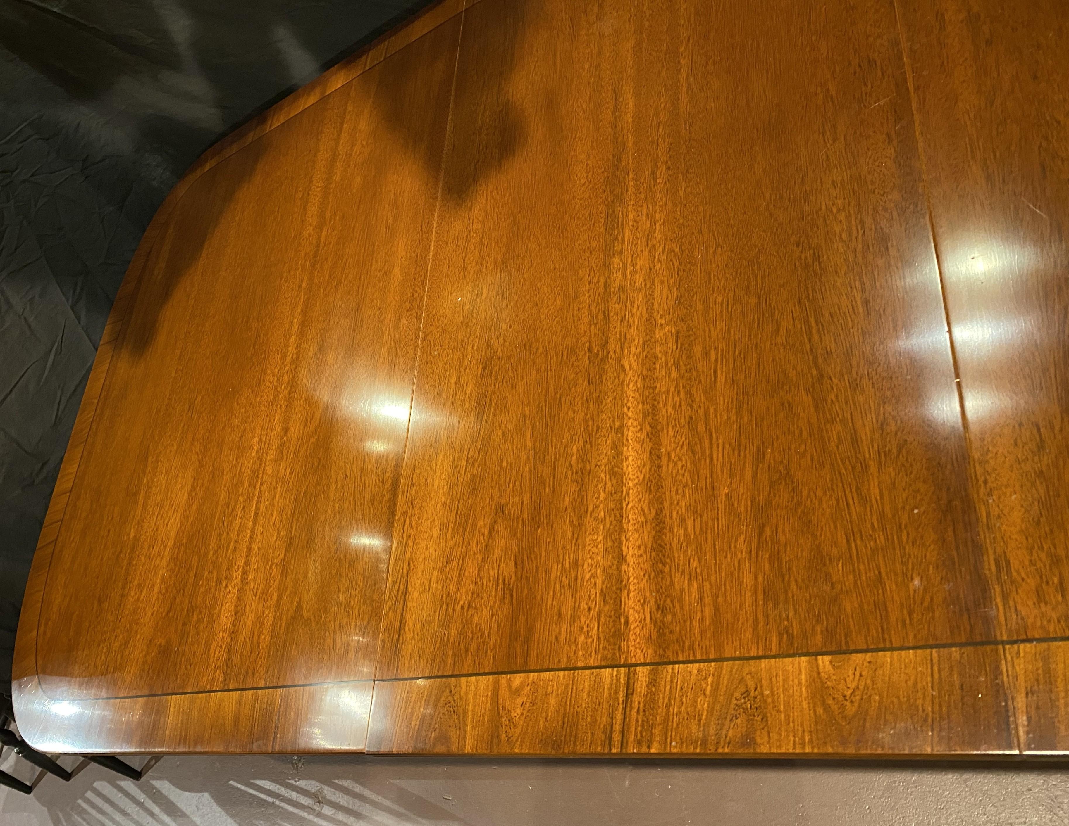 A fine Georgian style mahogany dining table with cross-banded veneer border, rounded corners, supported by two turned tripod pedestals with down swept legs, terminating with brass foot caps and casters. English in origin, dating to the 20th century,