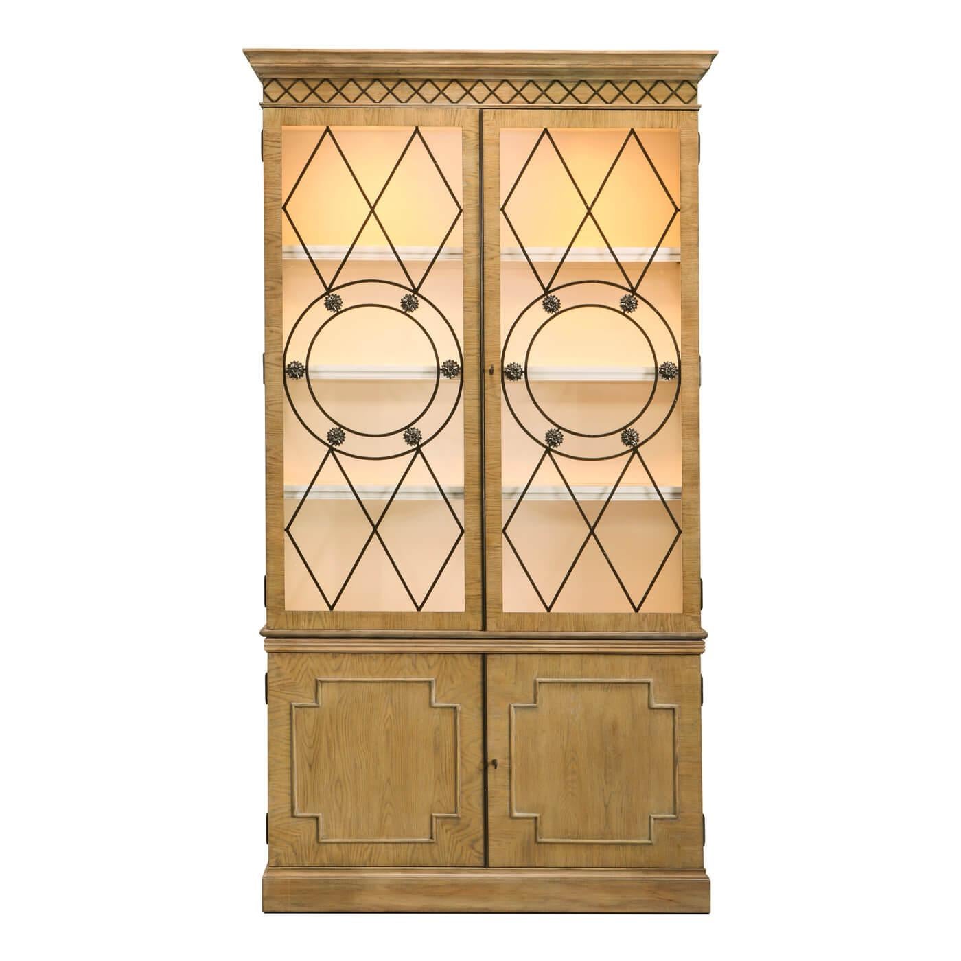 An updated and modern English Georgian-style oak bookcase or display cabinet with glass doors and brass accents. Cast rosettes are placed to separate circular bands in the center of the door grille. This design is inspired by early 19th century