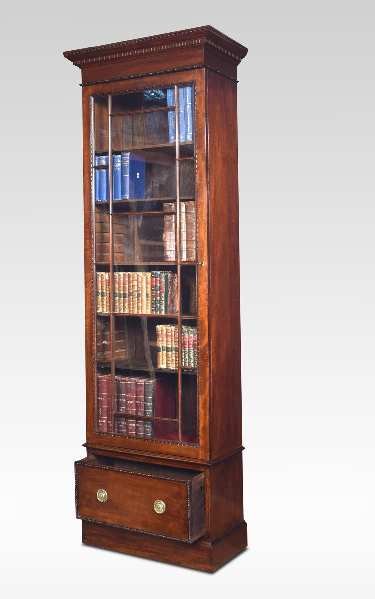 Georgian style tall narrow bookcase The projecting dentil moulded cornice above large astragal glazed door, opening to reveal an adjustable shelved interior. To the base fitted with single drawer and brass circular handles. All raised up on a