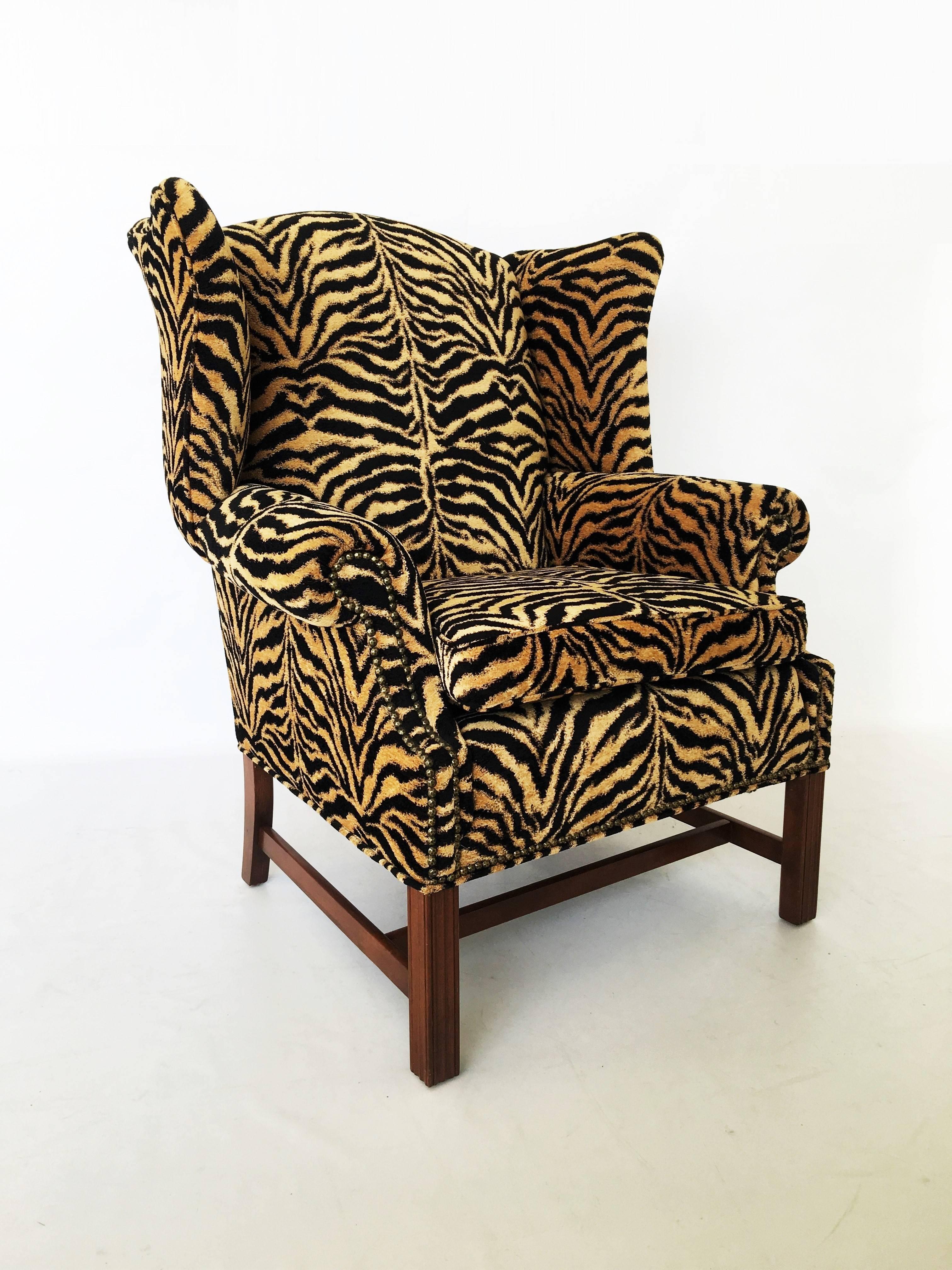 Beautiful Georgian style tiger print upholstered wingback chair. This chair features a curved crest rail and wing panels joining flared armrests. This piece includes a removable seat cushion over an upholstered apron with brass nailhead trim. The