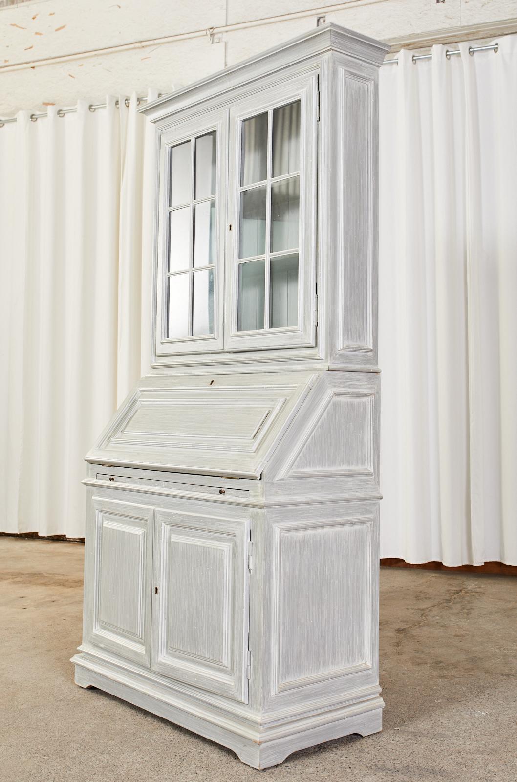 Painted English Georgian style two-piece secretaire bookcase featuring a slant front or drop front desk. The top section has two paneled glass doors opening to a three shelf interior. The drop front opens to a large writing surface with two small