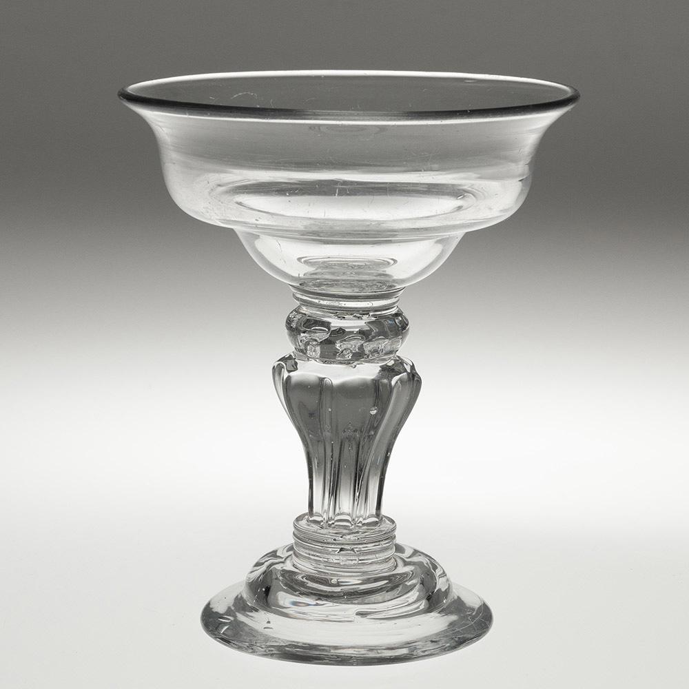 Encabezamiento : Vaso de golosina georgiano con pie de pedestal
Periodo : Jorge II
Origen : Inglaterra
Color : Transparente
Cazoleta : Doble conopial con borde evertido
Vástago : Bola aplanada de cuentas sobre pedestal de ocho lados con lágrima de