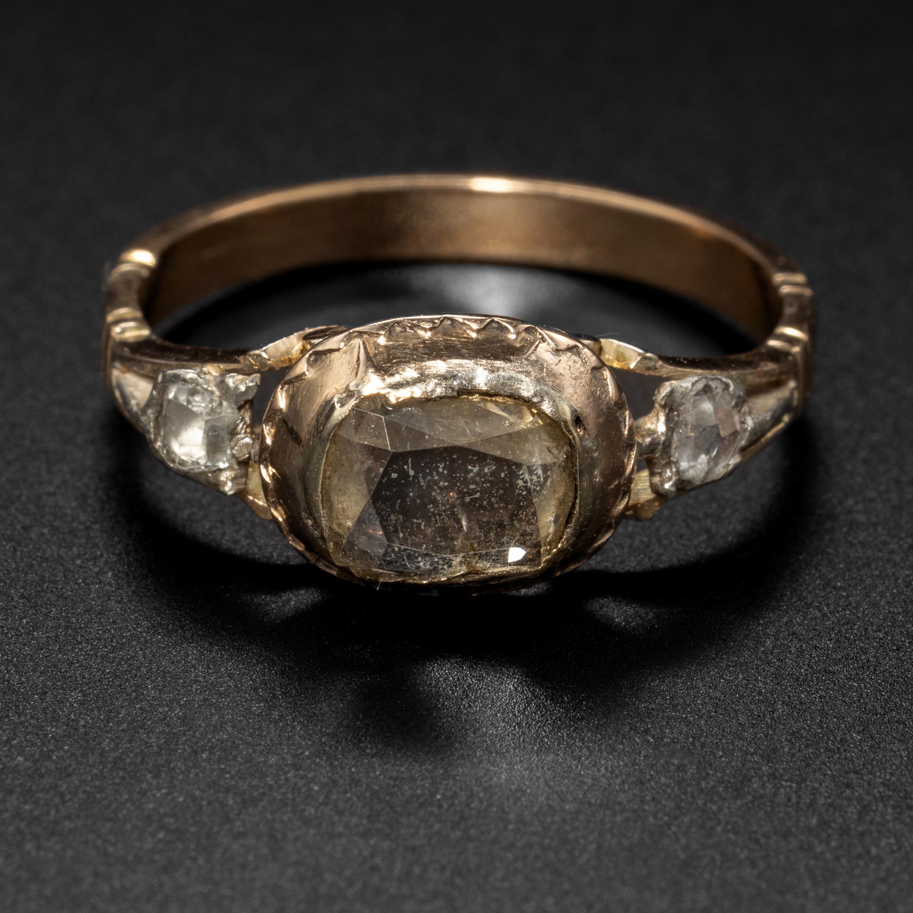 This Georgian-era 14K gold and silver ring features a sizeable -and quite rare- table cut diamond. The closed-back setting prevents an accurate measurement of the stone but it appears to be at least 1 carat. Two and rocky little rose-cut diamonds
