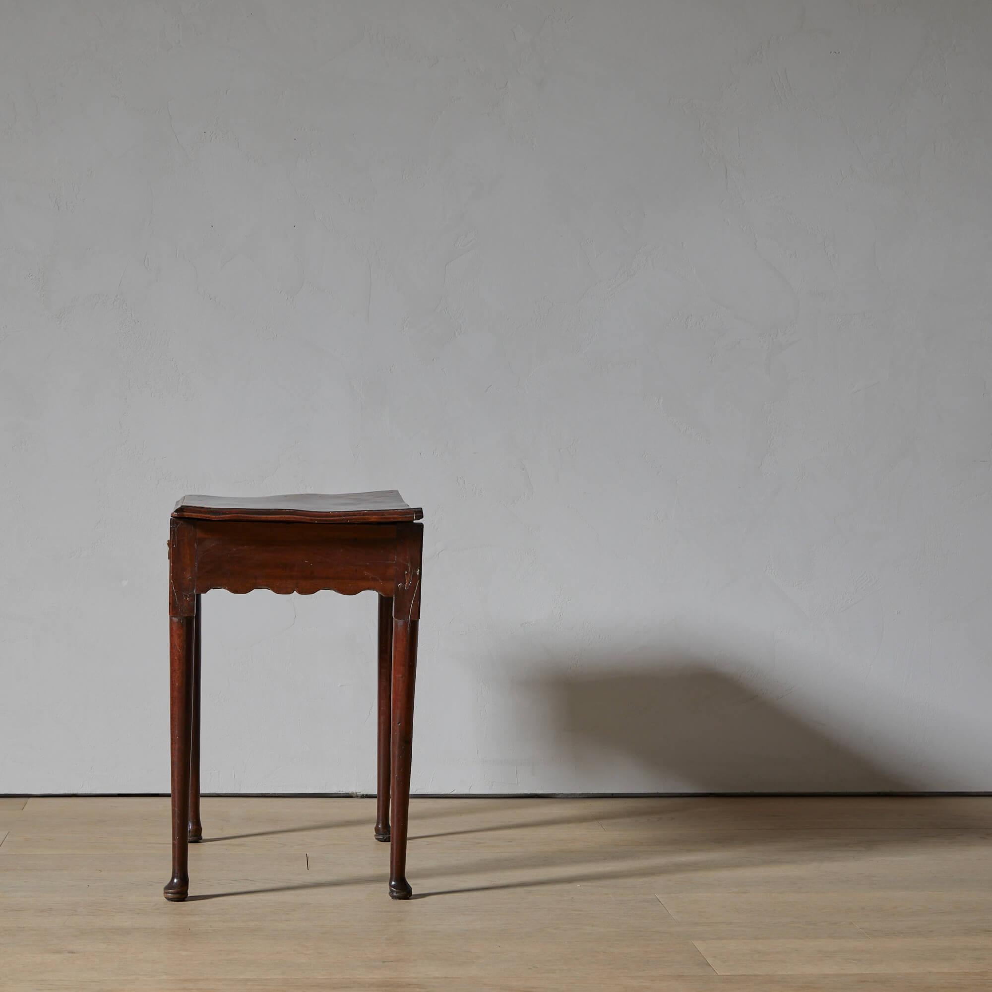Un tavolino o tavolo da scrittura risalente all'epoca di Giorgio II, che dimostra la sua età in modo eccellente. Soprattutto la parte superiore, nel suo stato deformato e ondulato, premia la mano. Adoriamo il grembiule intagliato e le gambe