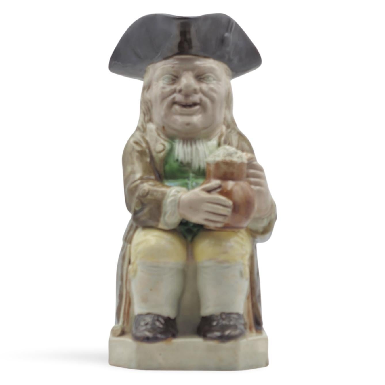 Fina jarra toby temprana, de la familia de alfareros Wood. Forma tradicional, sentada y sosteniendo una jarra espumosa de cerveza, vestida con ropas de la época.

Las jarras Toby se originaron a mediados del siglo XVIII en Staffordshire. El nombre