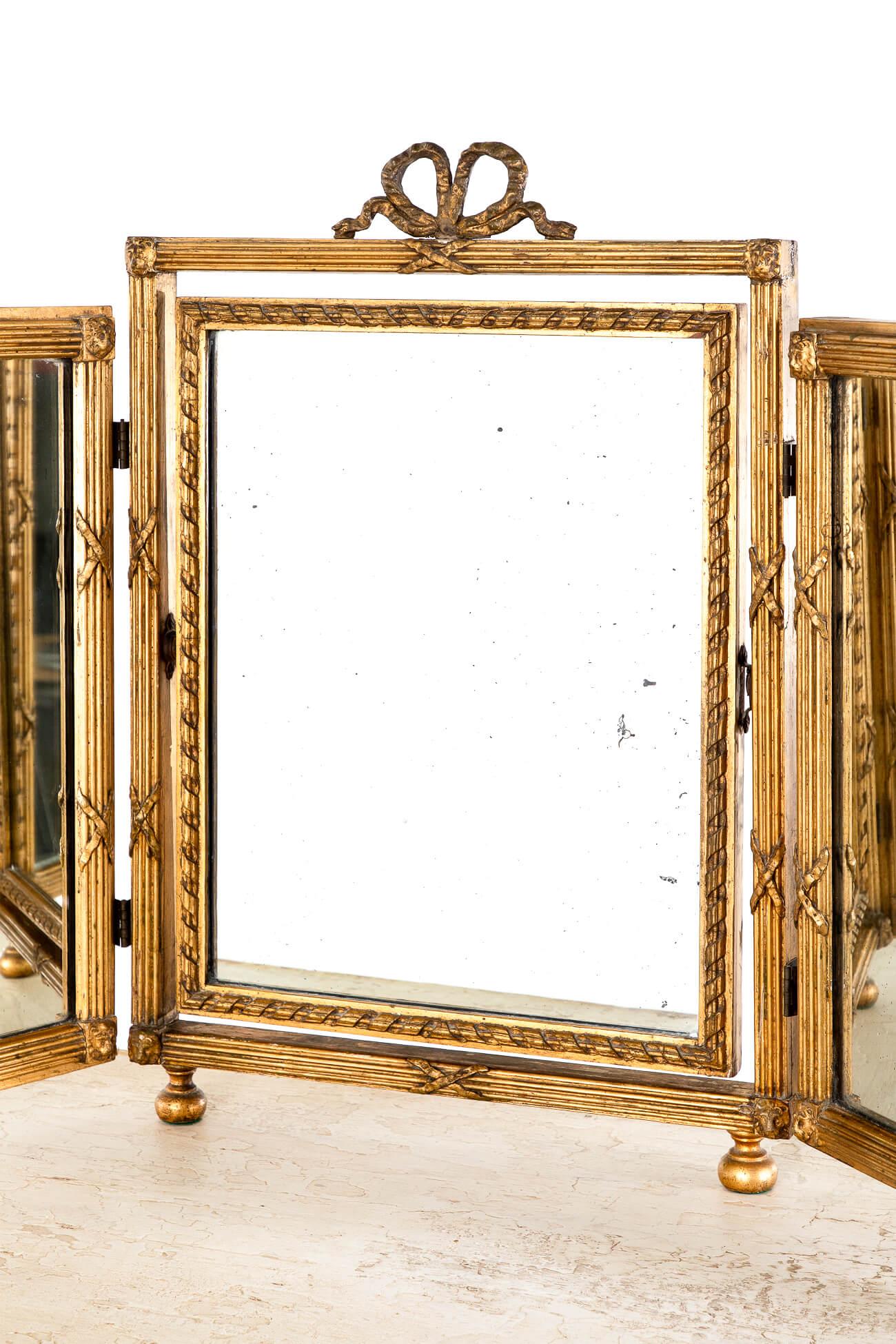 A fabulous late Georgian triptych gilt dressing table mirror in wonderful condition.

The frame to the gently foxed mirror plates is adorned with rams heads and Regency style bows.

The frame displays the original backing and resting on gilt bun