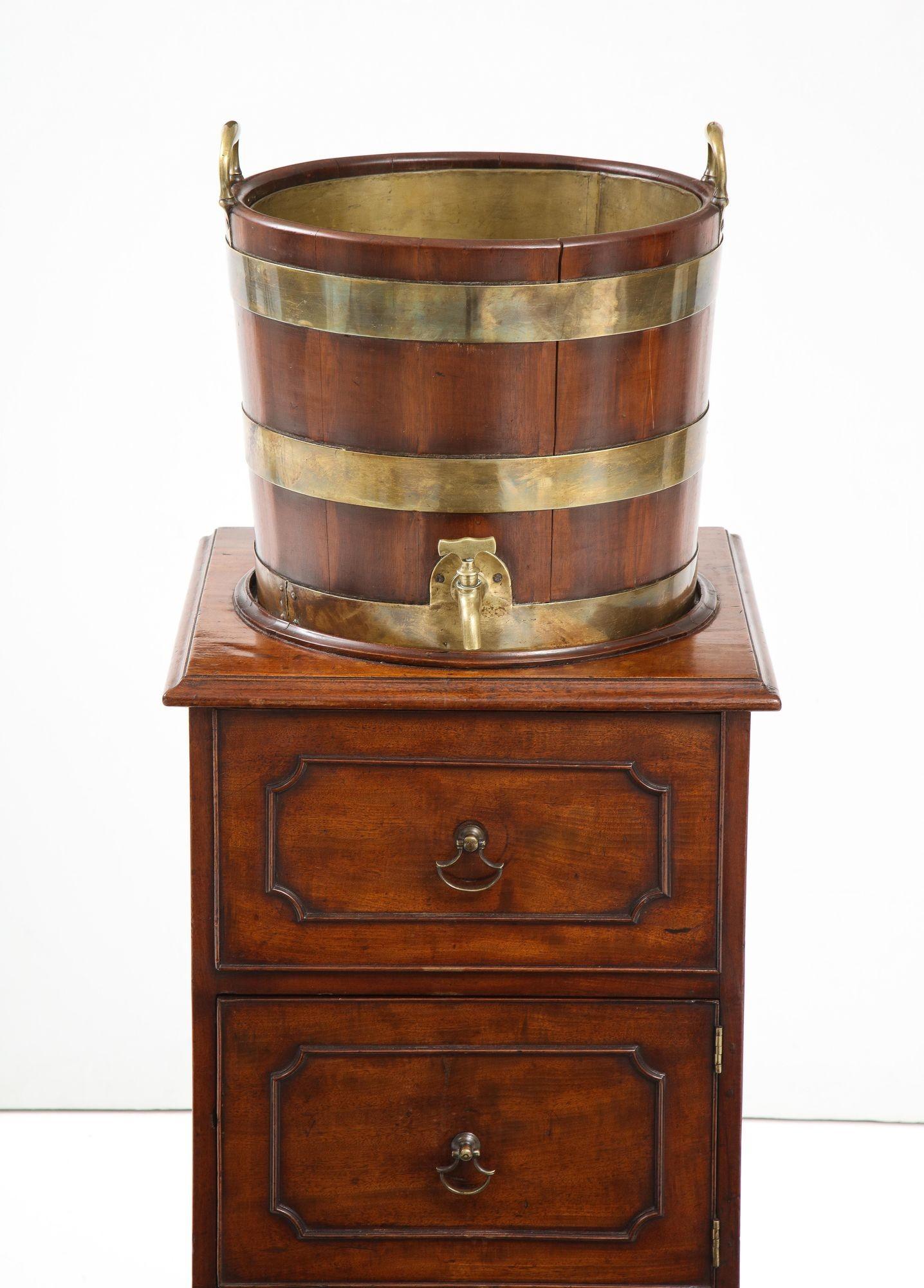 Very fine George III mahogany and brass bound wine cooler on original pedestal cabinet, the cooler with original brass handles and other mounts standing on three-compartmented cabinet, the top with molded recess over shaped drawer, the second