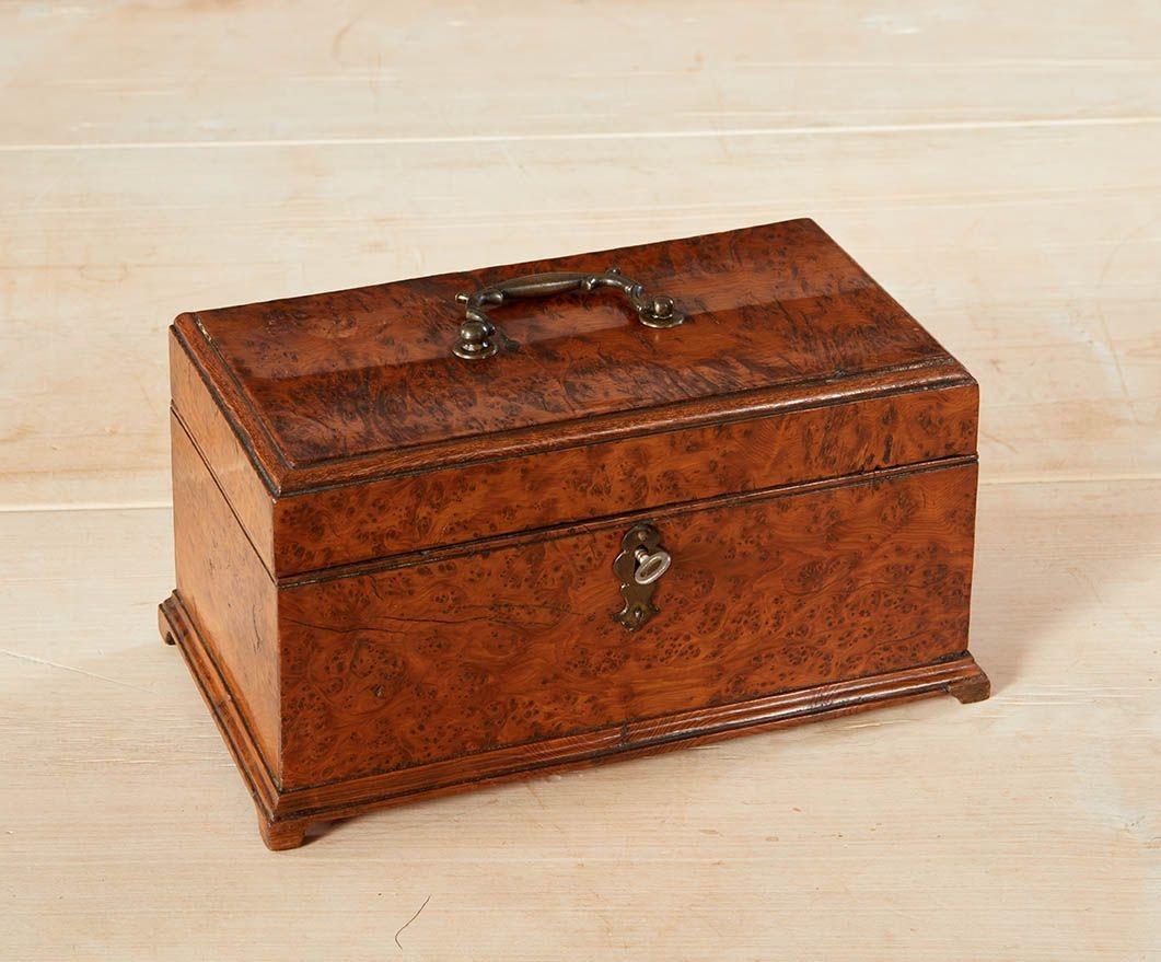 Caja de madera maciza de tejo Jorge III, con asa de transporte original en forma de espolón y apoyada en pies de ménsula, interior con tres separadores y forrado con papel marmolizado original.