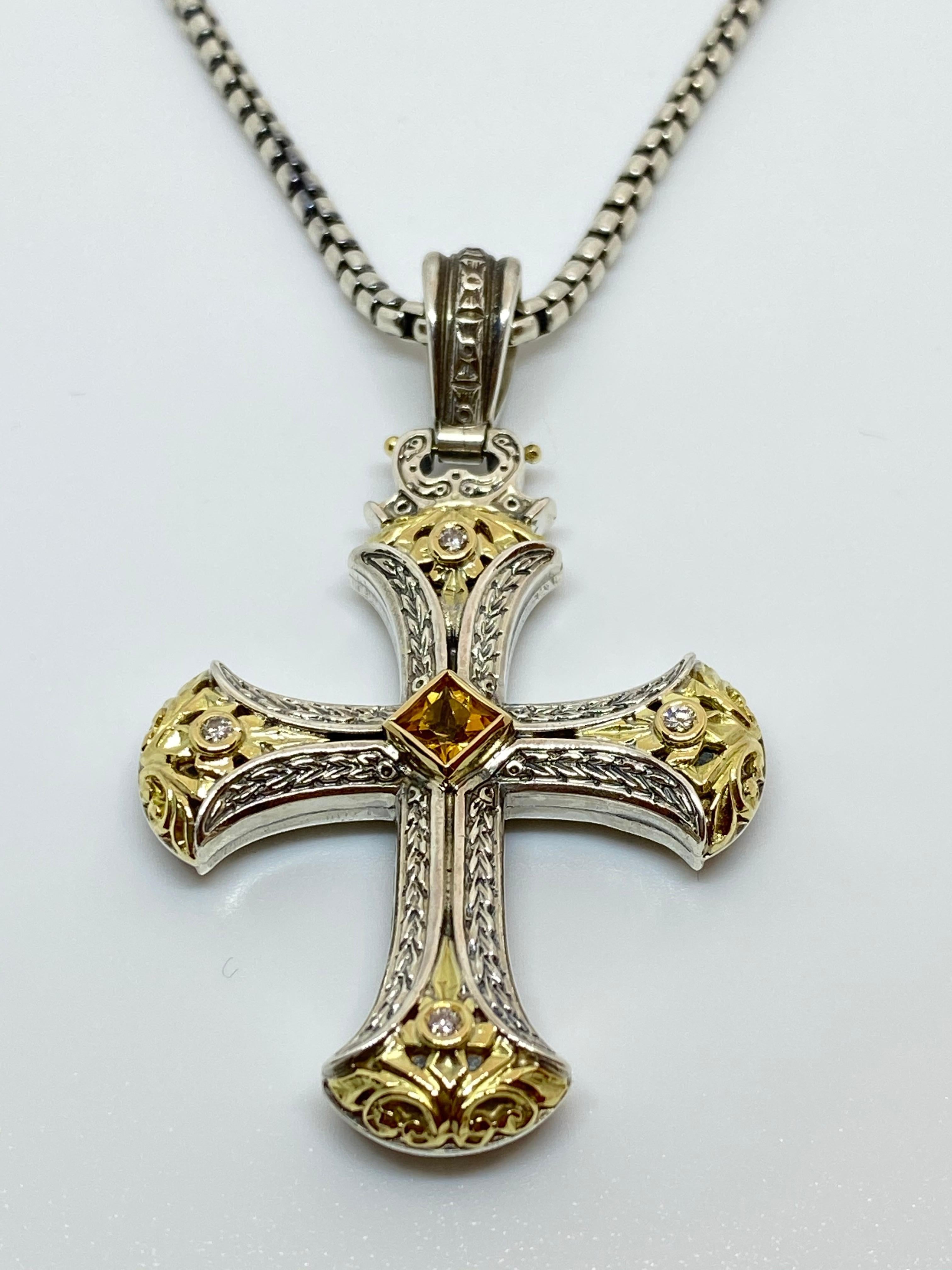 S.Georgios designer Silver and Gold 18 Karat two-tone Cross pendant is crafted from solid 18 Karat yellow gold pieces inlaid to create a unique look. This gorgeous cross enhancer features 4 Diamonds total weight of 0.16 Carat and a yellow Sapphire