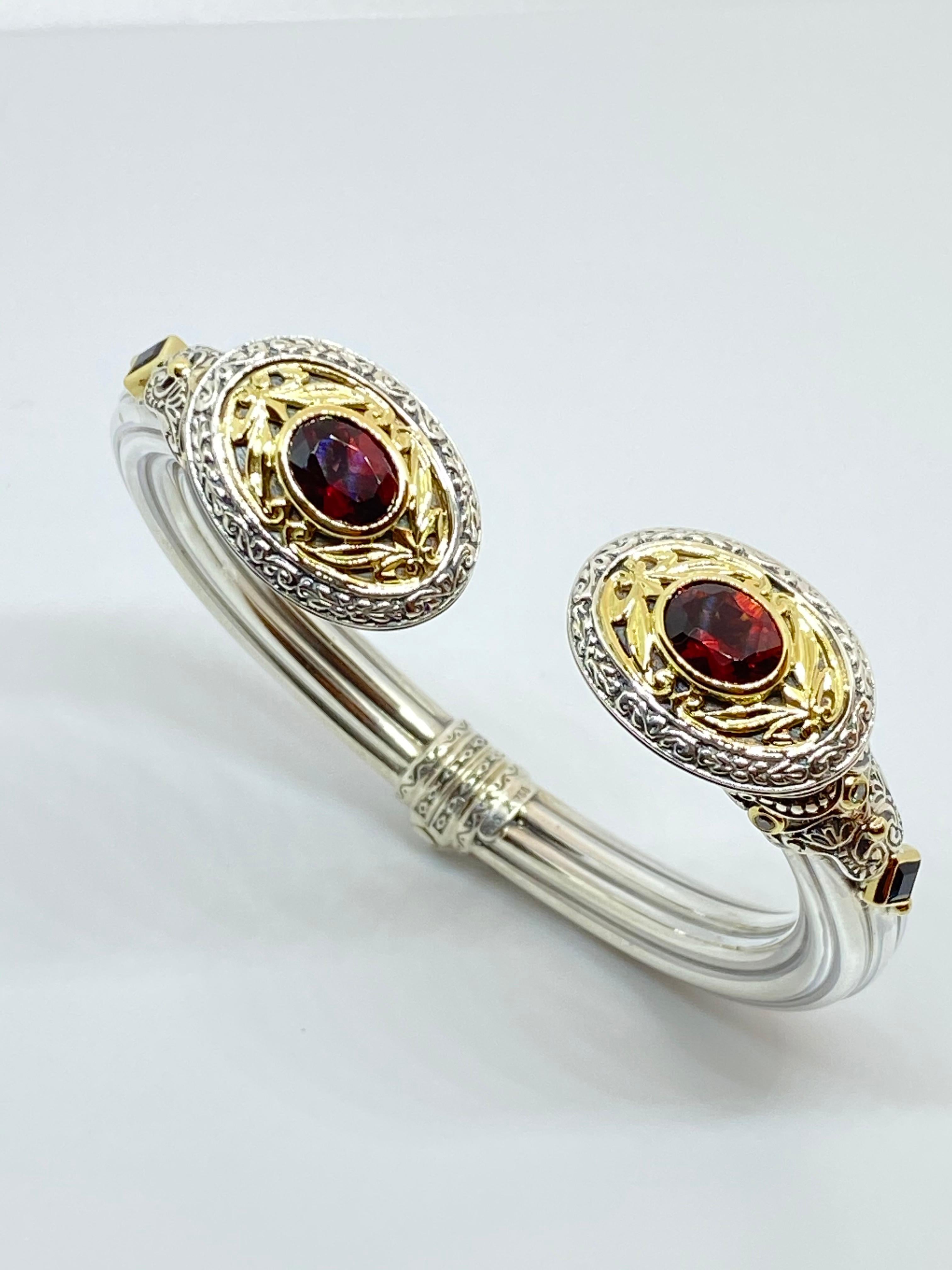 Questo bracciale di design S.Georgios in argento e oro giallo a 18 carati è realizzato a mano e presenta 2 granati rossi dal taglio ovale per un peso totale di 2,78 carati. Questo splendido bracciale è impreziosito da 2 zaffiri blu taglio