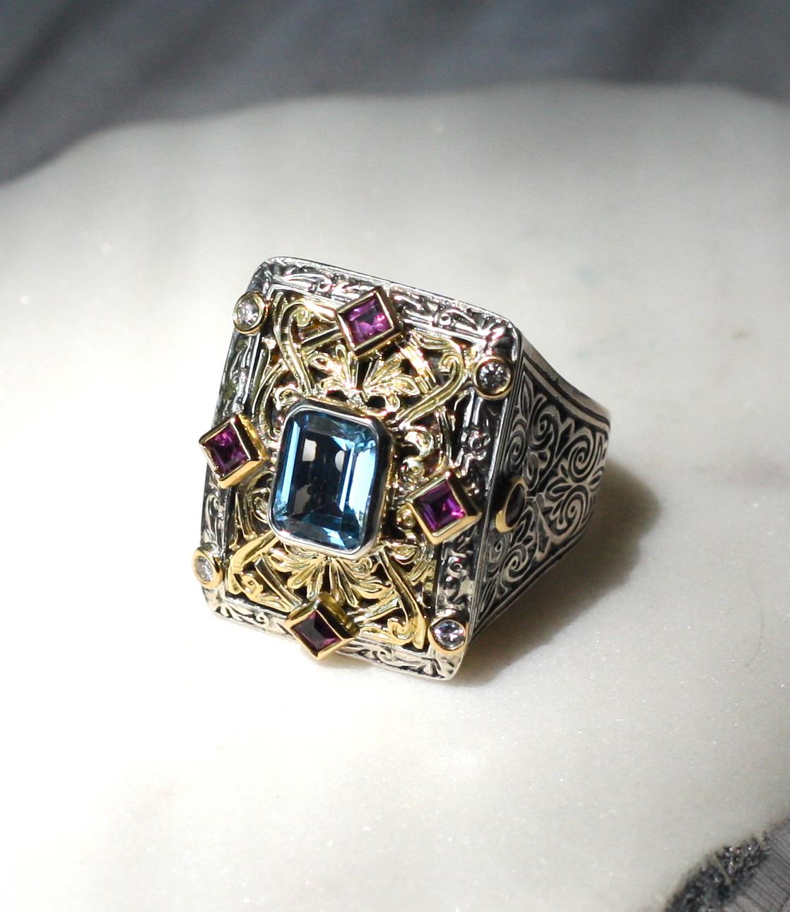 Il designer S.Georgios presenta anelli decorati pesanti fatti a mano, realizzati in argento sterling e oro giallo massiccio da 18 carati per creare un look unico. Questo splendido anello presenta una tormalina blu taglio smeraldo al centro, 4