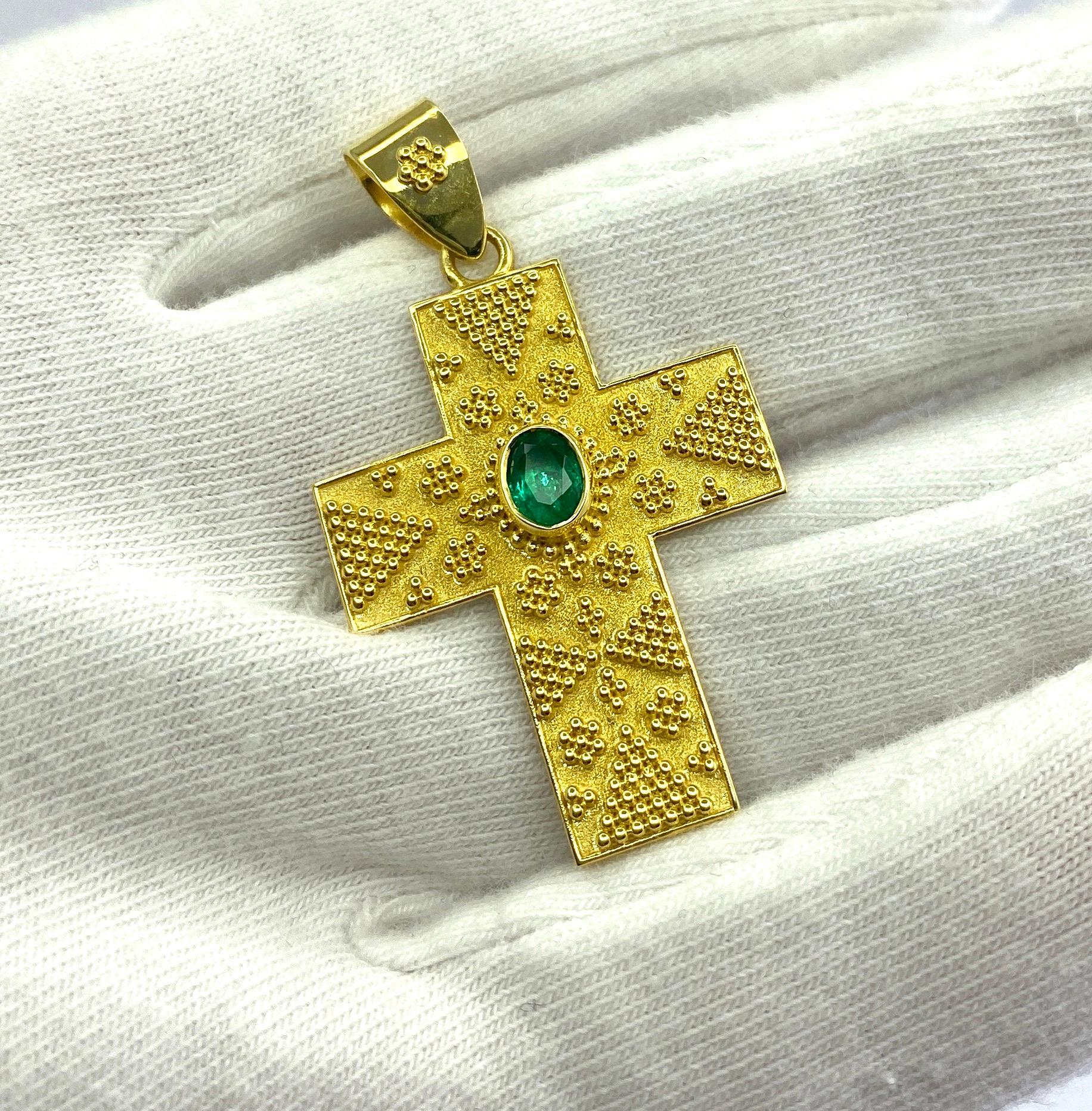 This S.Georgios Designer Byzantine Style Cross is handmade from solid 18 Karat Yellow Gold. It is heavily decorated with granulation work and features 0.30 Carat oval shape Emerald on the velvet background. This art piece is made in outstanding
