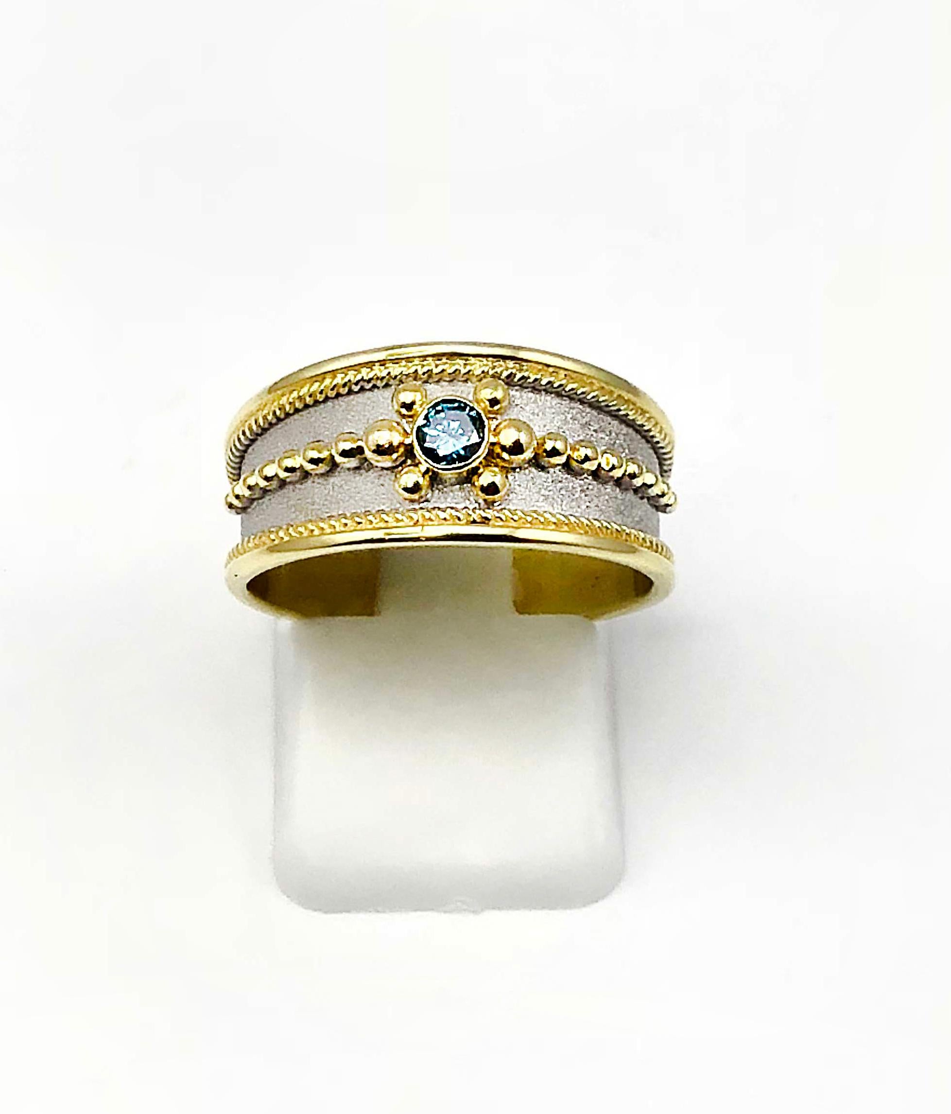S.Georgios designer Band Ring in Yellow Gold 18 Karat all decorated with Byzantine-style granulation and a unique velvet background finished in White Rhodium. The center of the ring features a Blue Diamond total weight of 0.12 Carat.
This gorgeous