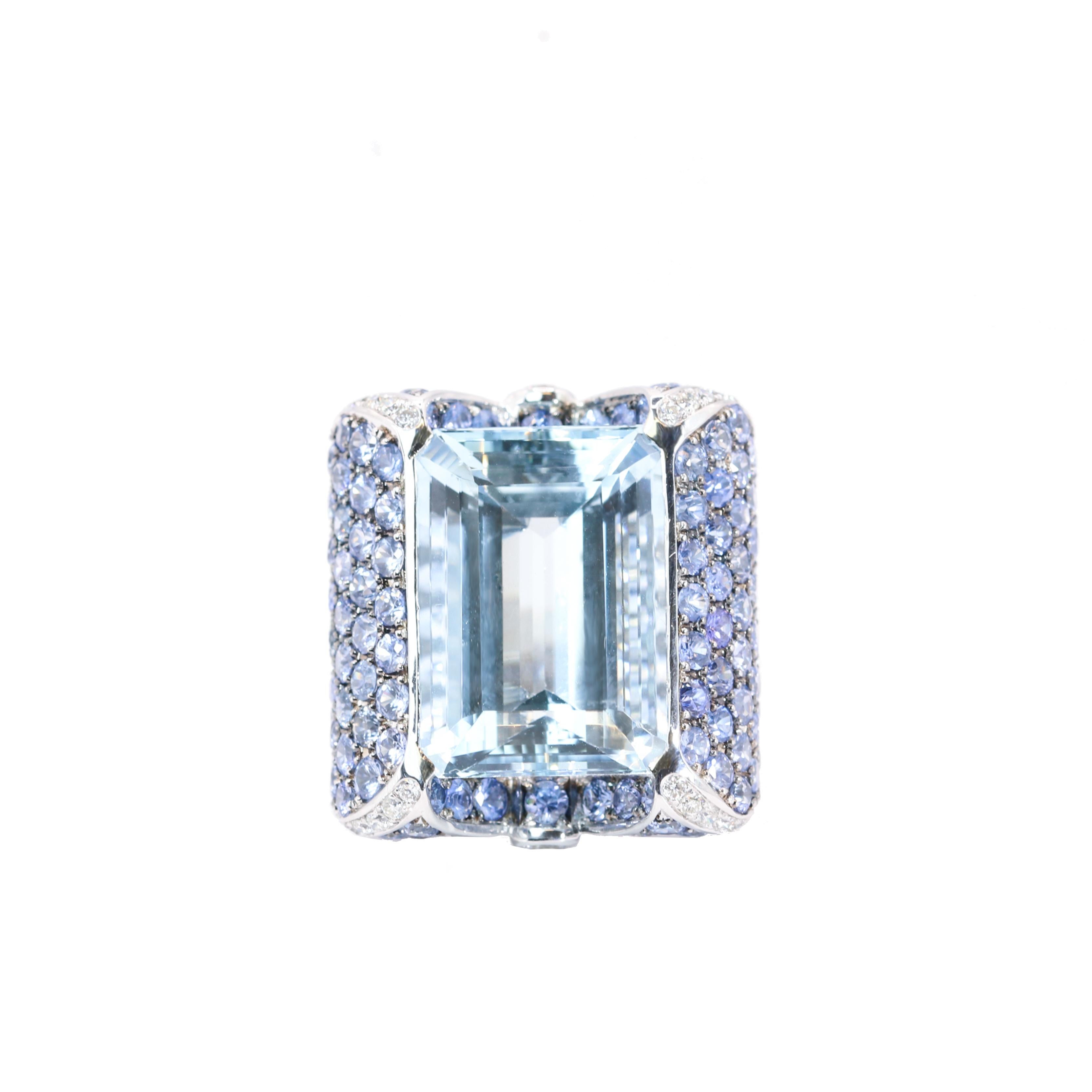 S.Georgios designer presents a magnificent 18 Karat White Gold Ring featuring a 15.70 Carats  emerald-cut Aquamarine at the center, surrounded by an array of Sapphires total weight of 8.16 Carats on the band and White Diamonds total weight of 0.80