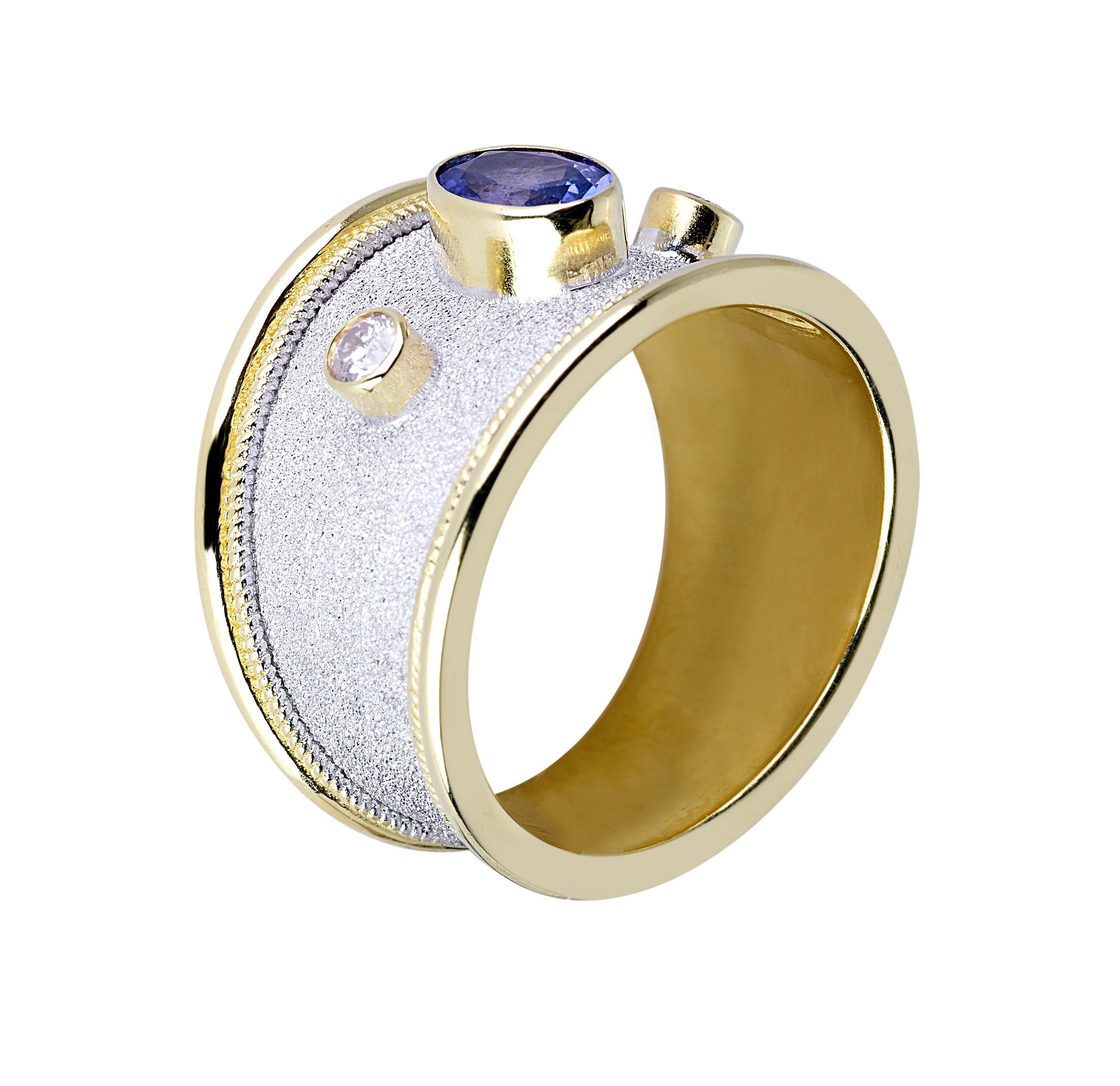 S.Georgios Designerring ist aus massivem 18 Karat Gelbgold handgefertigt und maßgefertigt. Der wunderschöne Ring zeigt einen Tansanit und 2 Diamanten im Kontrast zu einem Hintergrund aus byzantinischem Samt, der in weißem Rhodium ausgeführt ist. Das