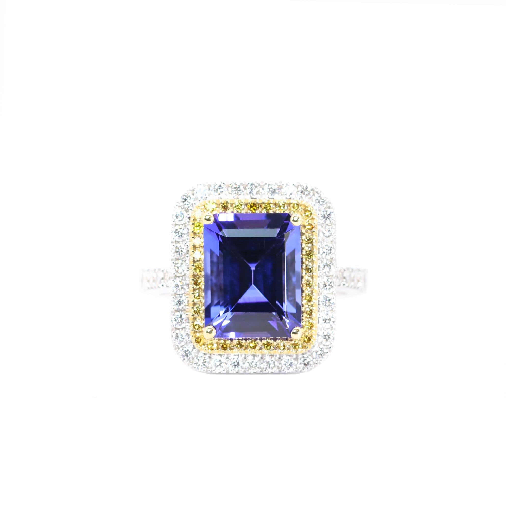 S.Georgios designer presents an exquisite 18 Karat White Gold ring featuring an emerald-cut 5.99 Carats Tanzanite at its center, framed by a dazzling bezel of Yellow and White Diamonds, total weight of 0.21 and 0.65 Carats respectively . The