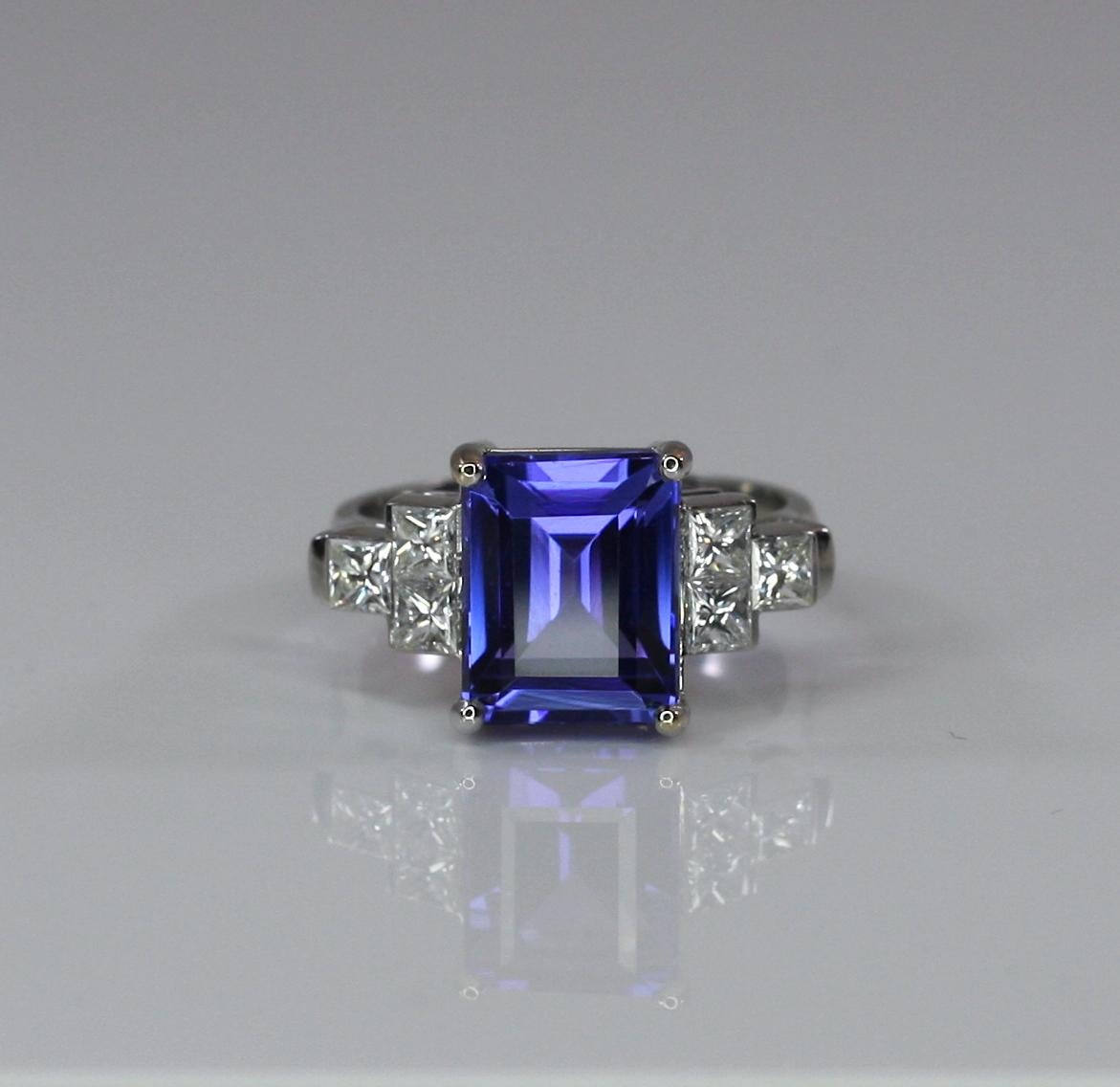 S.Georgios designer ring with an emerald-cut Tanzanite and princess cut Diamonds. This gorgeous ring is handmade from 18 Karat White gold in Athens Greece and features a 6.01 Carat Natural Tanzanite in precise cut, accompanied by 6 invisible set