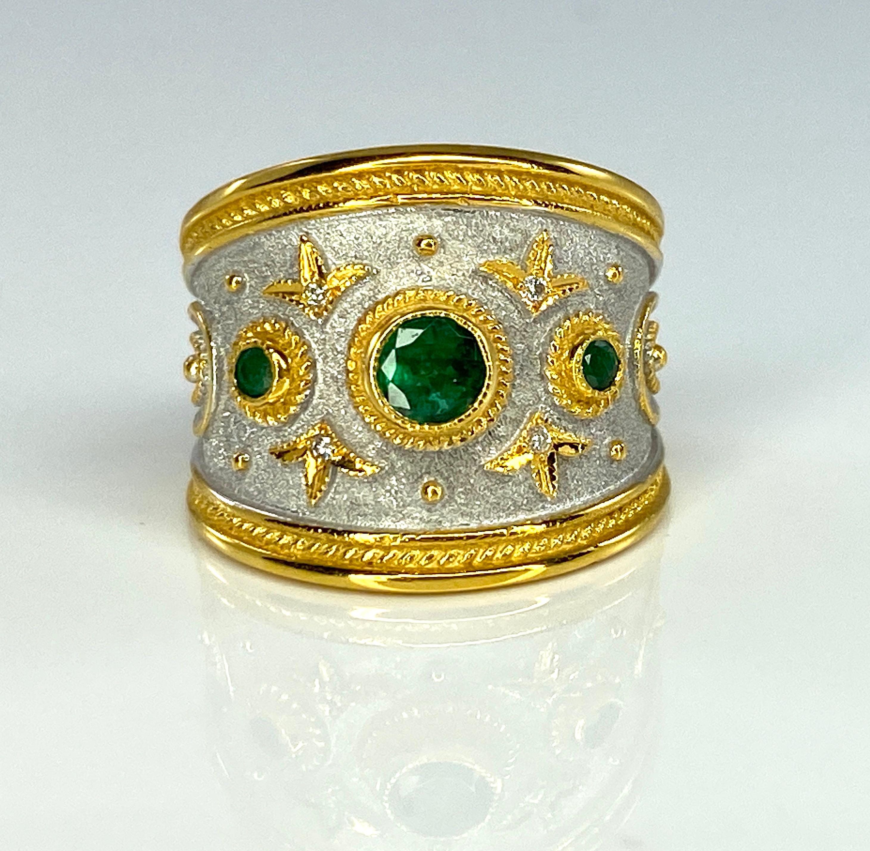 S.Georgios designer 18 Karat Yellow Gold Ring is handmade in Byzantine Style - decorated with granulation that stands out from a velvet background which is finished with White Rhodium. The ring features 3 Brilliant cut Emeralds with a total weight