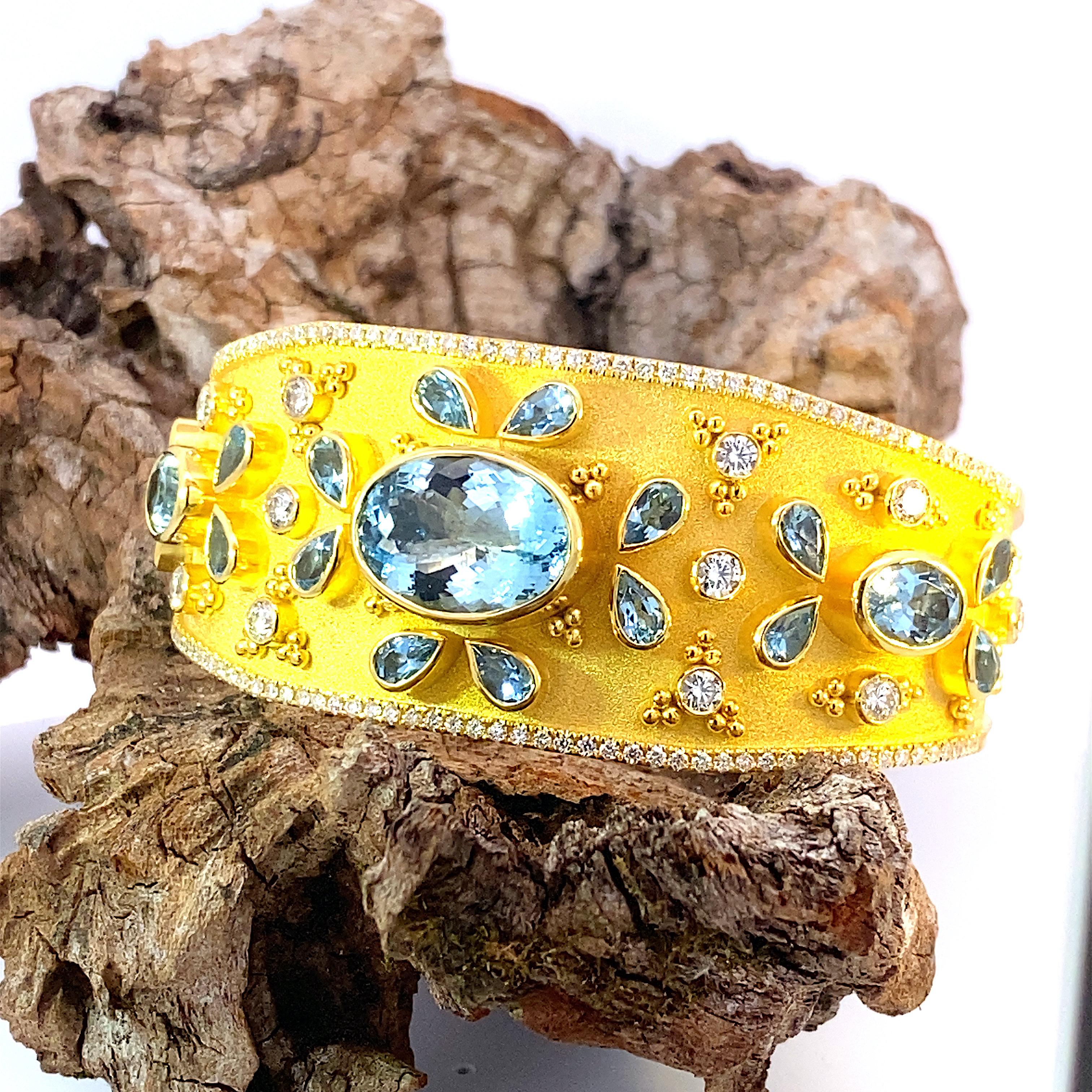 S.Georgios Unique designer bangle bracelet handmade in solid 18 Karat yellow gold. This bracelet is finished in a unique Byzantine-style velvet texture on the background and granulation work. The bracelet features 3 oval cut Aquamarines with a total