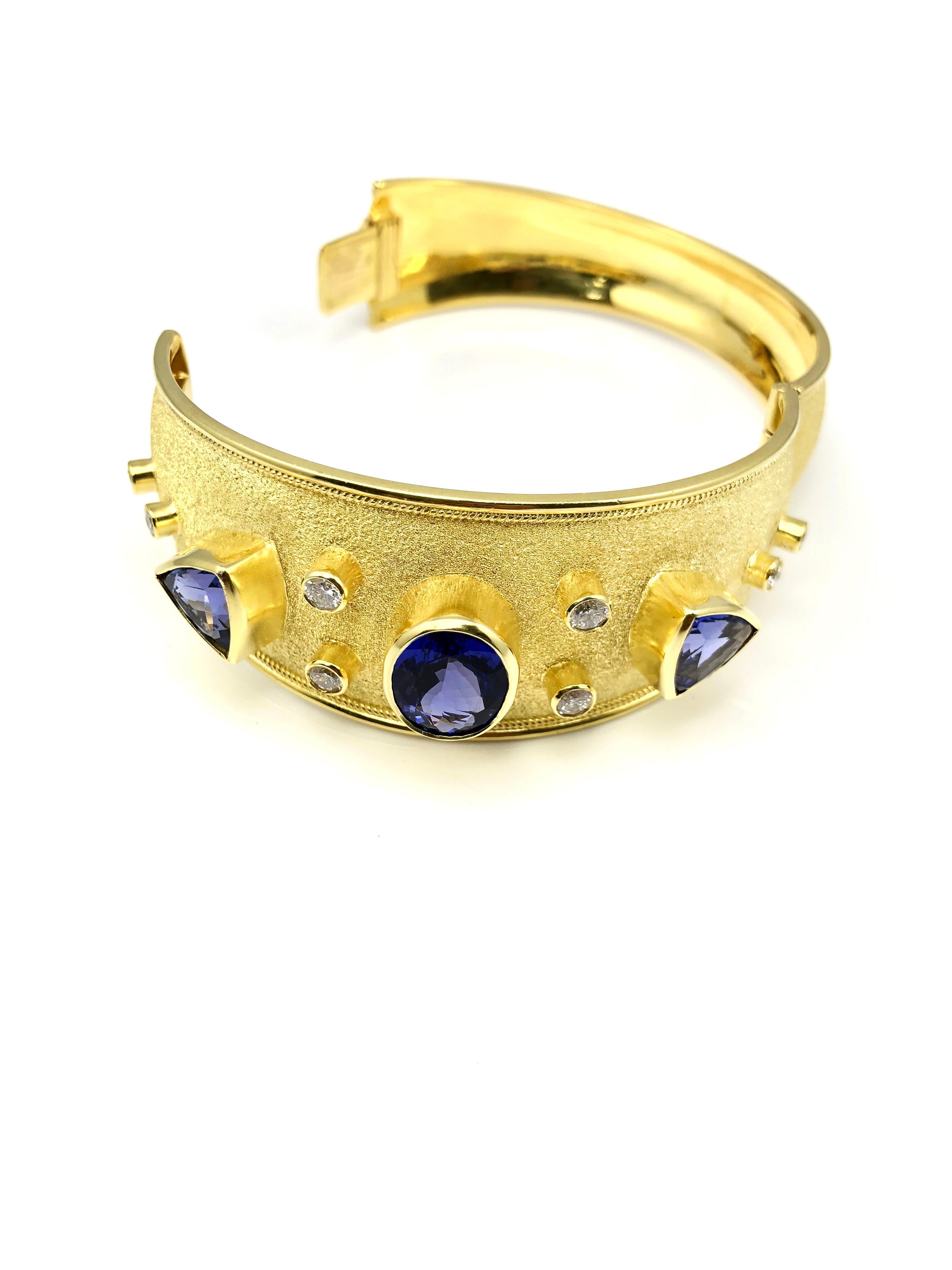 S.Georgios designer Bangle Bracelet is handmade from solid 18 Karat Yellow Gold all custom-made. This beautiful bracelet in its simplicity features Oval and Triangular Shape Tanzanites and 8 Diamonds on a unique Byzantine velvet background. The