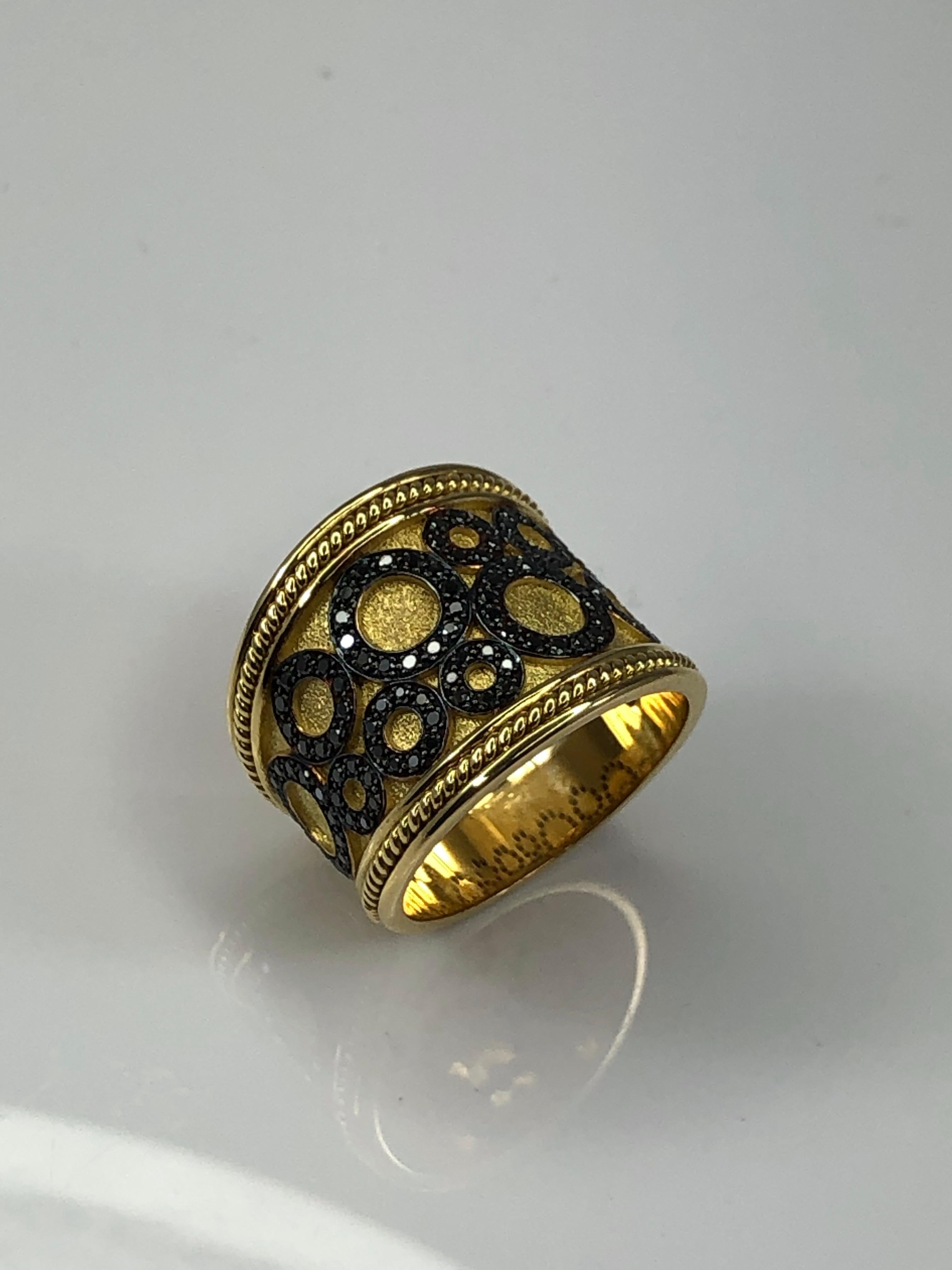 Voici la bague design de S.Georgios faite à la main en or jaune 18 carats en Grèce. Cette bague combine l'ancienne technique byzantine avec un design moderne. Sur un fond de velours se détache un ensemble de cercles décorés de diamants noirs d'un
