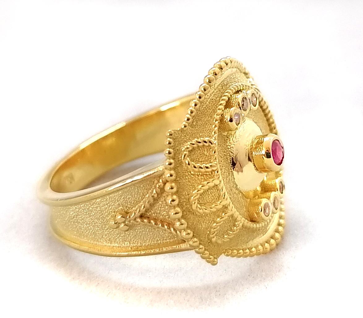Cette bague de créateur S.Georgios est fabriquée à la main en or jaune 18 carats massif. Cette magnifique bague ronde est décorée au microscope avec un travail de granulation de style byzantin et présente un élégant rubis taille brillant d'un poids