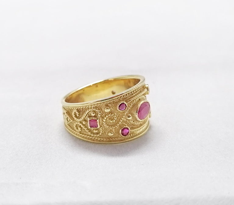 This S.Georgios designer 18 Karat Yellow Gold band Ring is all handmade with bead granulation workmanship and a unique velvet background. This gorgeous band ring features a center Oval cut natural Ruby, framed by 6 Multi-cut Rubies all with a total
