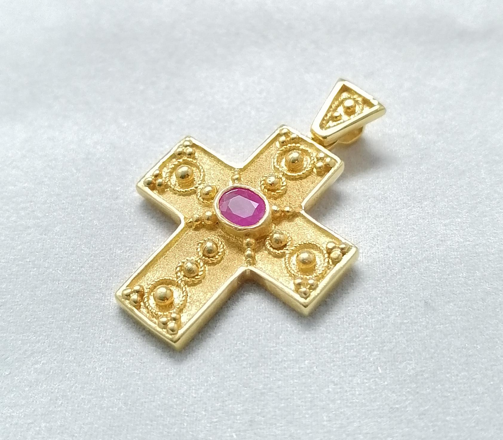 This S.Georgios solid 18 Karat Yellow Gold geometric Cross pendant is beautifully handmade and microscopically decorated Byzantine-style bead granulation work. This gorgeous cross features an oval-cut natural Ruby total weight 0.37 Carat and is