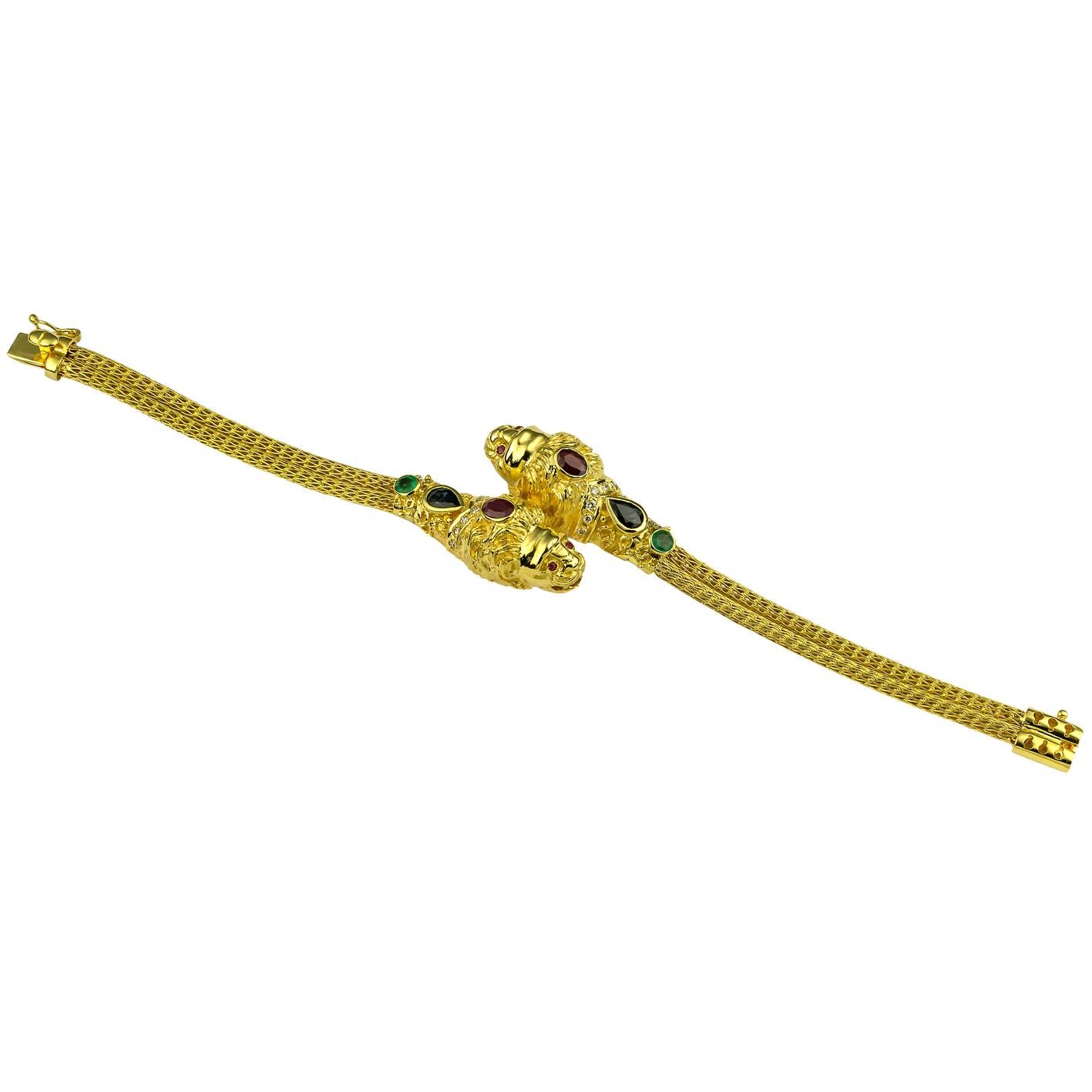 Dieses S.Georgios Doppel-Löwenkopf-Armband mit Diamanten, Rubinen, Saphiren und Smaragden ist aus massivem 18 Karat Gelbgold handgefertigt und mikroskopisch mit granulierten Details verziert. Dieses einzigartige Kunstwerk zeigt zwei Löwenköpfe mit