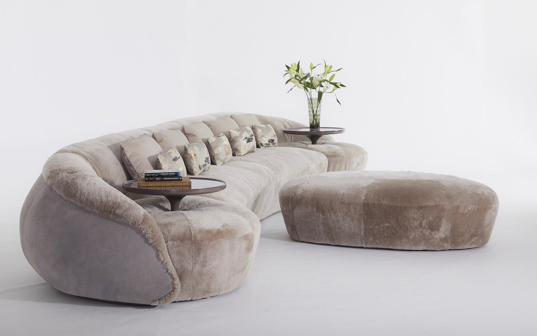 This monumental swoosh of a sofa includes two integral side tables and an ottoman. The ottoman can be flanked by two cocktail tables to create two seating groups. The fiberglass side tables can be removed for additional seating. Shown in shearling