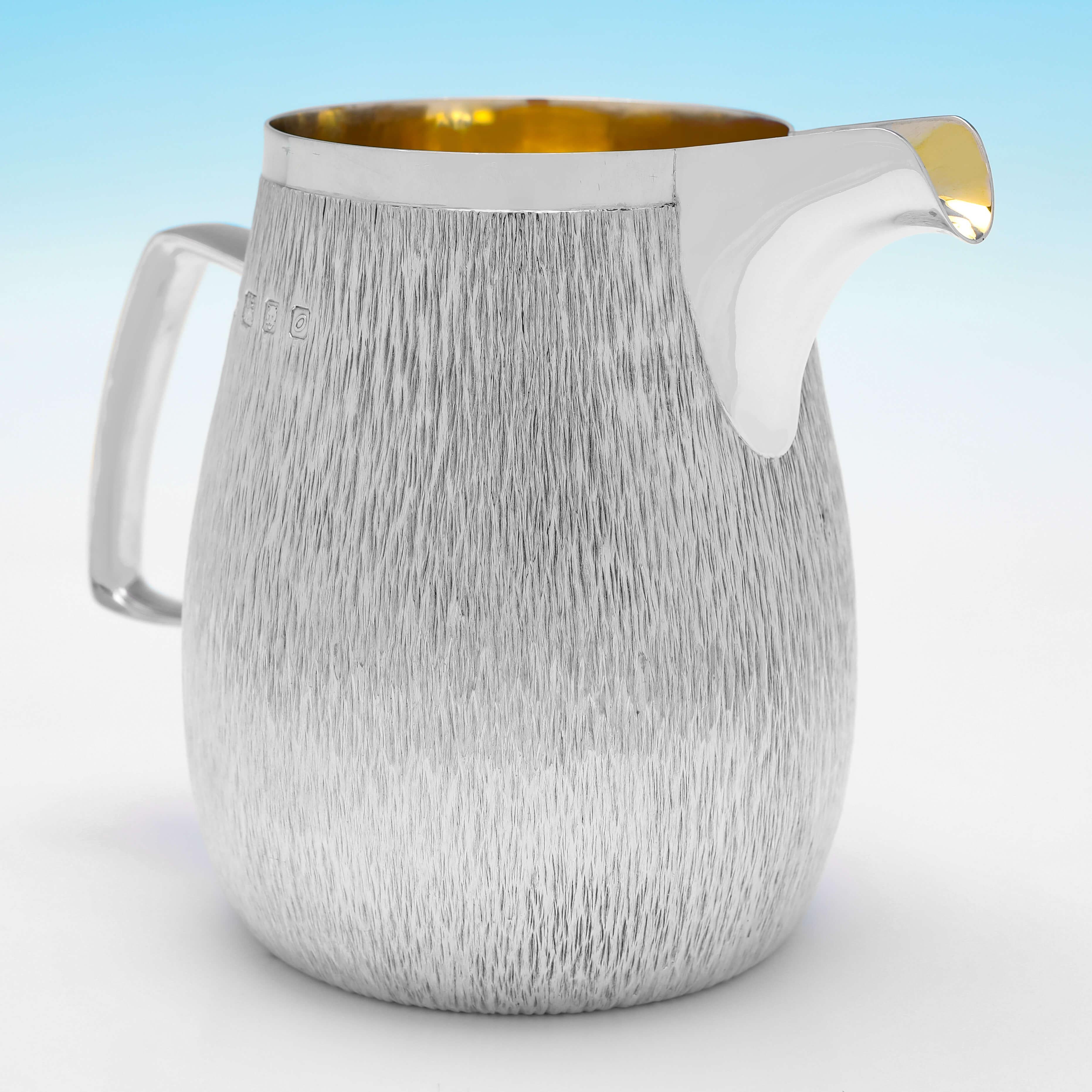 Hallmarked in London in 1969 by Gerald Benney, this very stylish, Sterling Silver Water Jug, features a gilt interior, and a bark effect finish. 

The jug measures 5.25