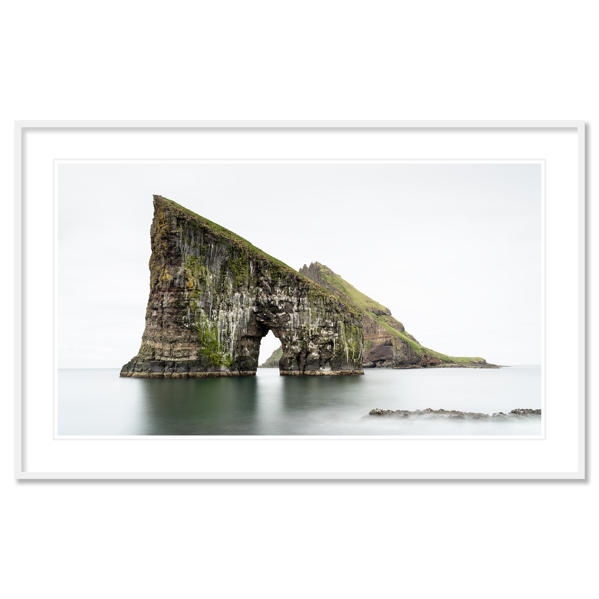 Gerald Berghammer - Farbige Seelandschaftsfotografie. Ein großer, mit Gras und Moos bewachsener Meeresstapel mit einem Bogen an der Basis, der sich aus dem ruhigen Wasser des Ozeans erhebt.
Pigmenttintendruck in einer limitierten Auflage von 8