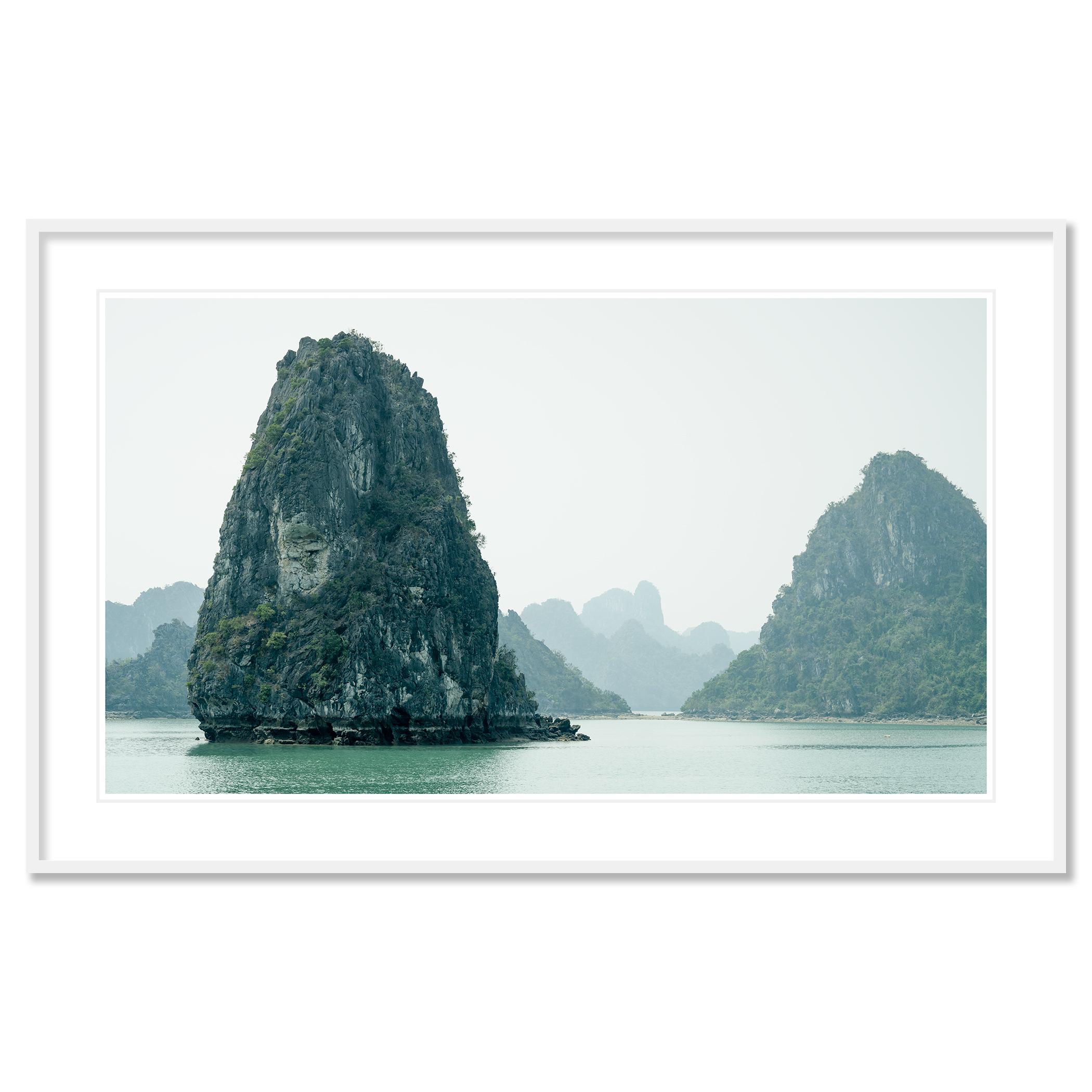 Gerald Berghammer - Photographie de paysages marins en couleur. Des formations karstiques calcaires émergent de l'eau dans une baie tranquille, avec des montagnes brumeuses, Asie du Sud-Est.
Tirage à l'encre pigmentaire d'archives faisant partie