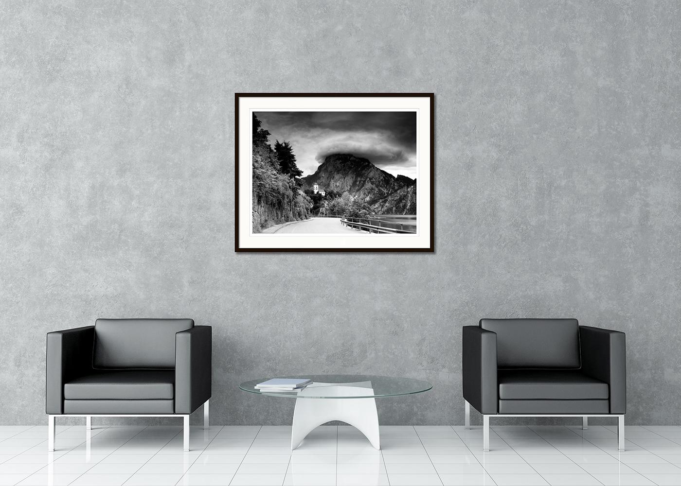 Photographie d'art en noir et blanc de paysages à longue exposition. Chapelle de Johannesberg avec les belles montagnes et le lac Traunsee par temps orageux avec des nuages gigantesques, Traunkirchen, Autriche. Épreuve à l'encre pigmentaire