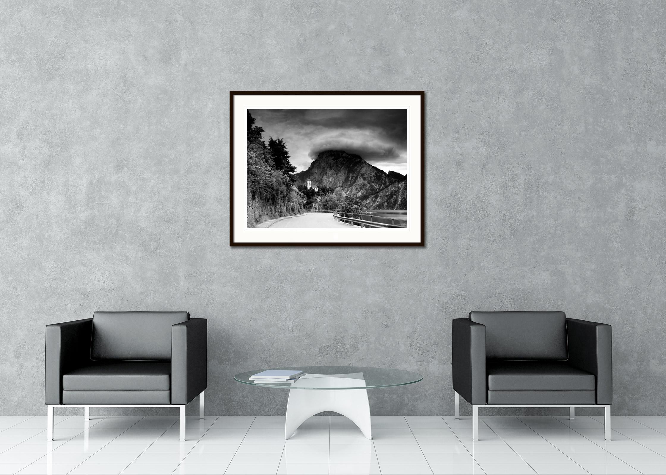 Photographie d'art en noir et blanc de paysages à longue exposition. Chapelle de Johannesberg avec les belles montagnes et le lac Traunsee par temps orageux avec des nuages gigantesques, Traunkirchen, Autriche. Épreuve à l'encre pigmentaire