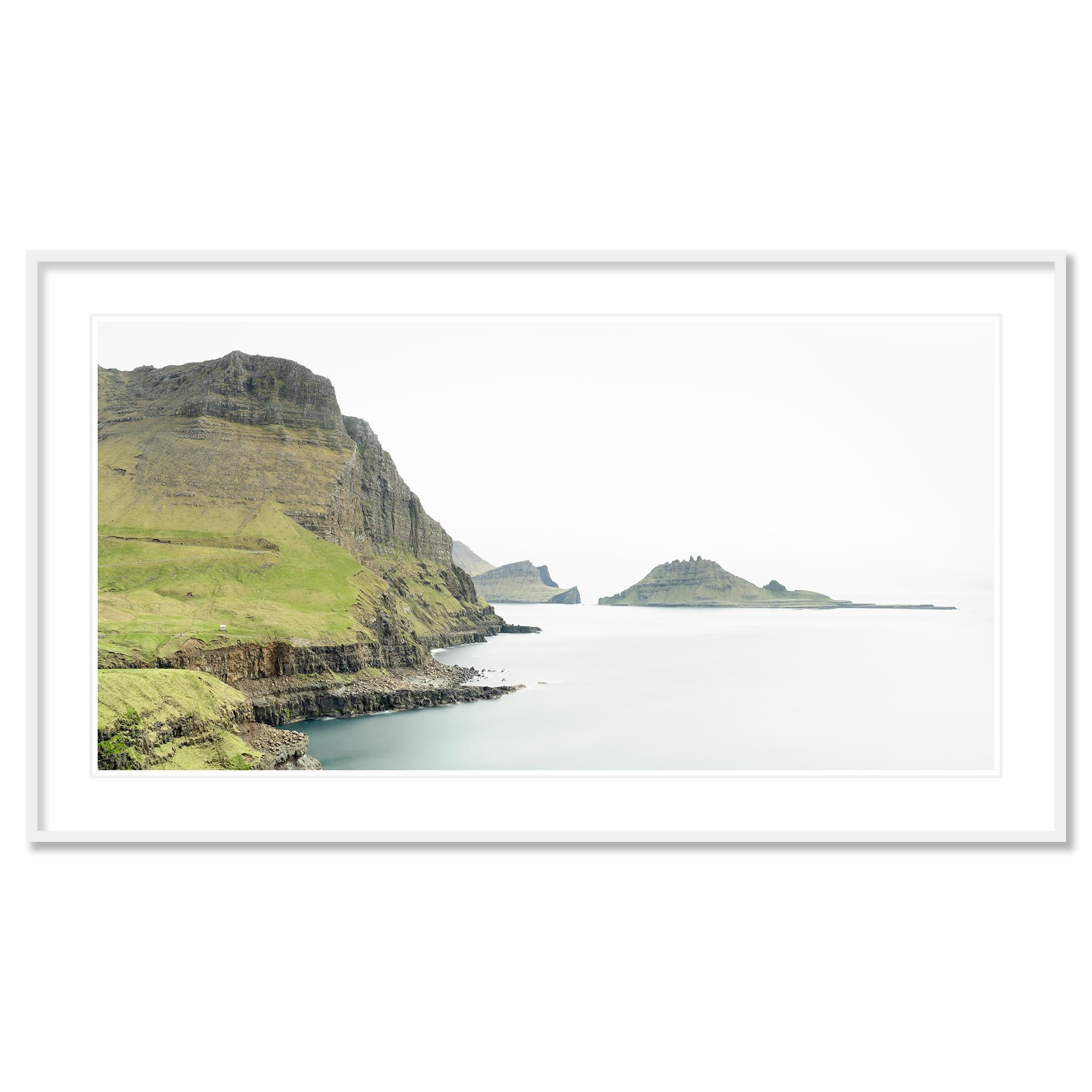 Gerald Berghammer - Photographie couleur. Falaises et collines verdoyantes le long d'une étendue d'eau, avec des îles ou des masses continentales lointaines en arrière-plan, sous un ciel nuageux.

Tous les tirages de Gerald Berghammer sont réalisés