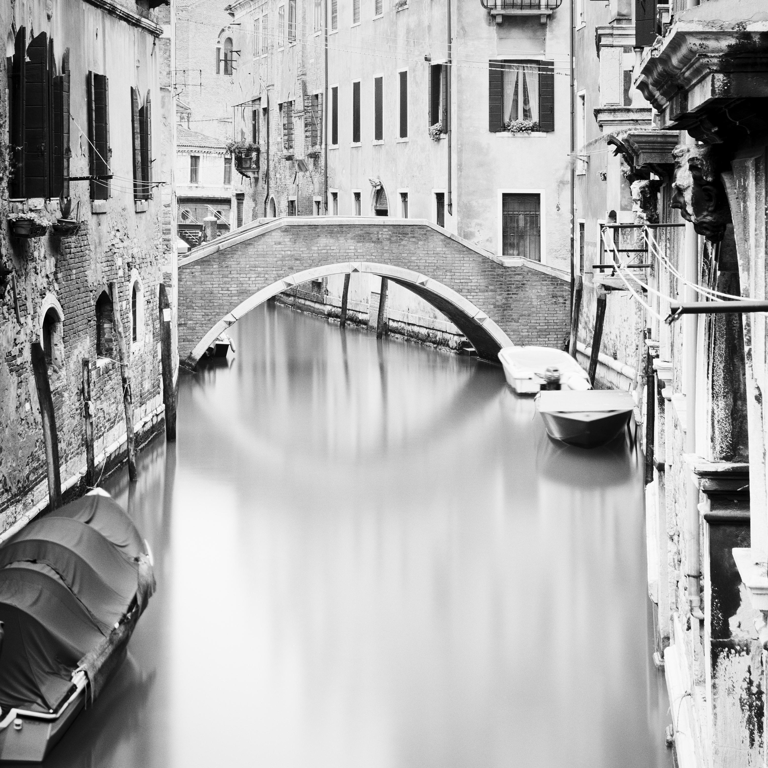 Black and White Fine Art Photography - Small stone bridge and a canal in Venice with boats. Archival pigment ink print, edition of 5. Signed, titled, dated and numbered by artist. Certificate of authenticity included. Printed with 4cm white