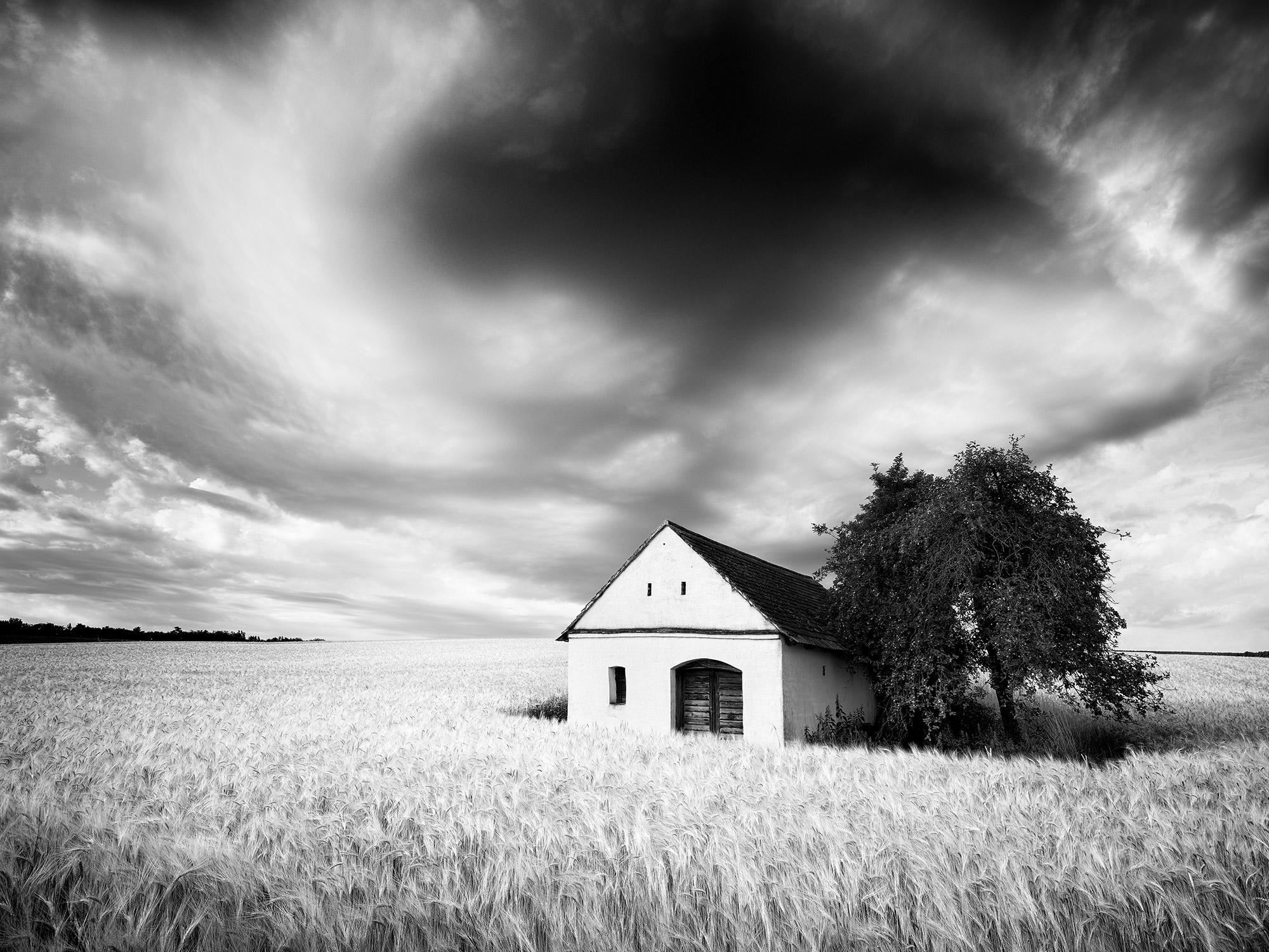 Gerald Berghammer Black and White Photograph - Wine Press House, wheat field, heavy cloud, black & white landscape photography