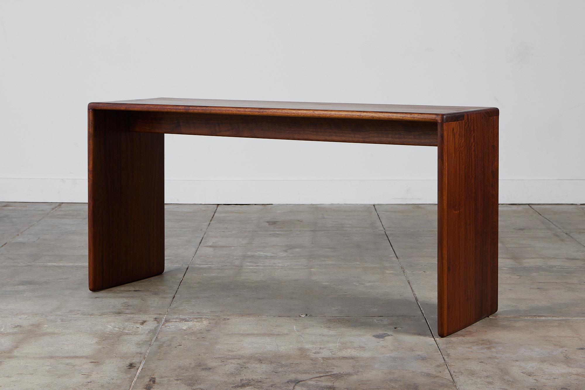 An American made console table, c.1970s, by Gerald McCabe is beautifully crafted from Shedua, also known as African Walnut. This piece features natural wood grain variances that cascade down the sides of the console. This piece would be perfect in