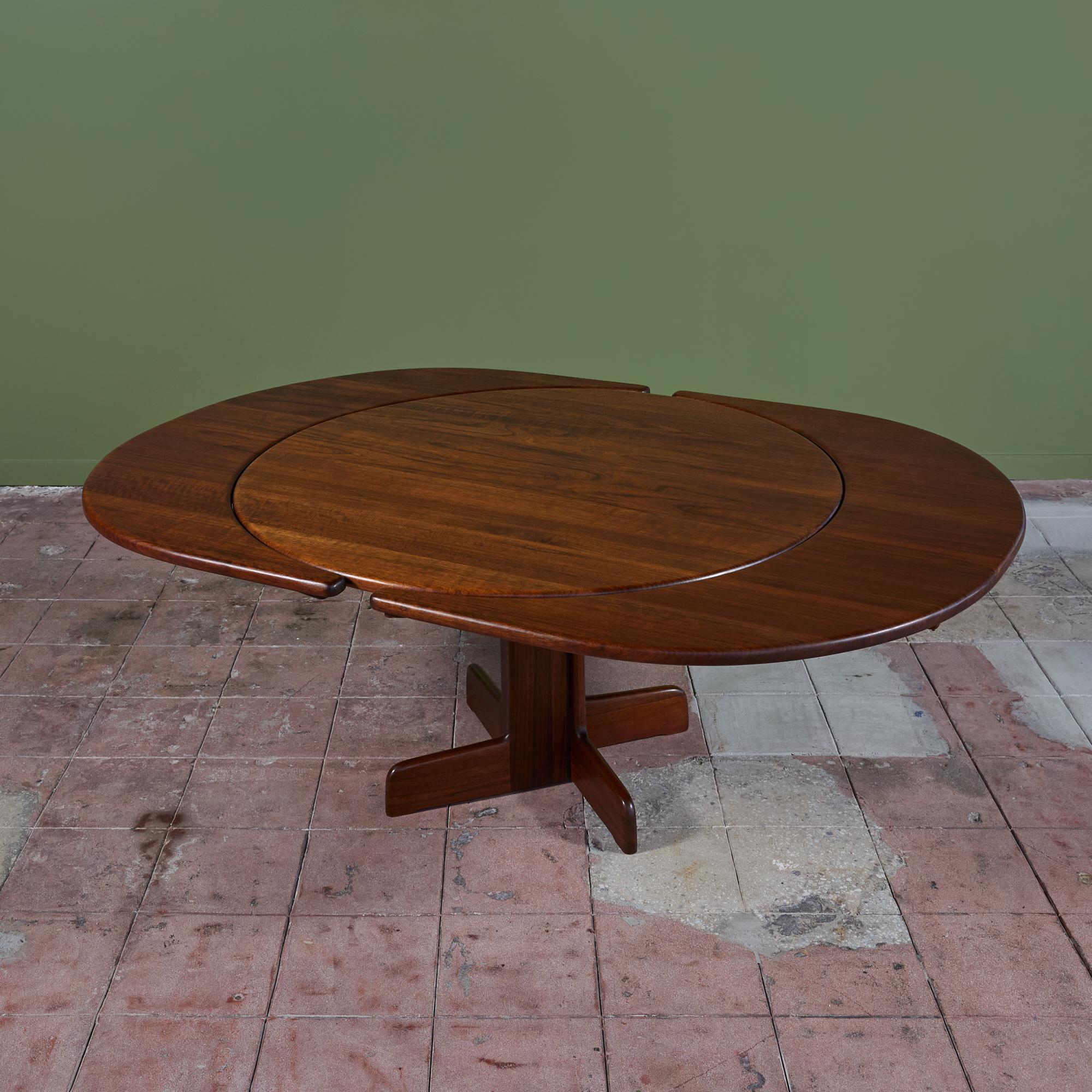 American made dining table, c.1970s, by Gerald McCabe. The table features a round top situated on a pedestal base made of solid Shedua. The table comes with two crescent leaves which attach to the outers sides of the table expanding to comfortably