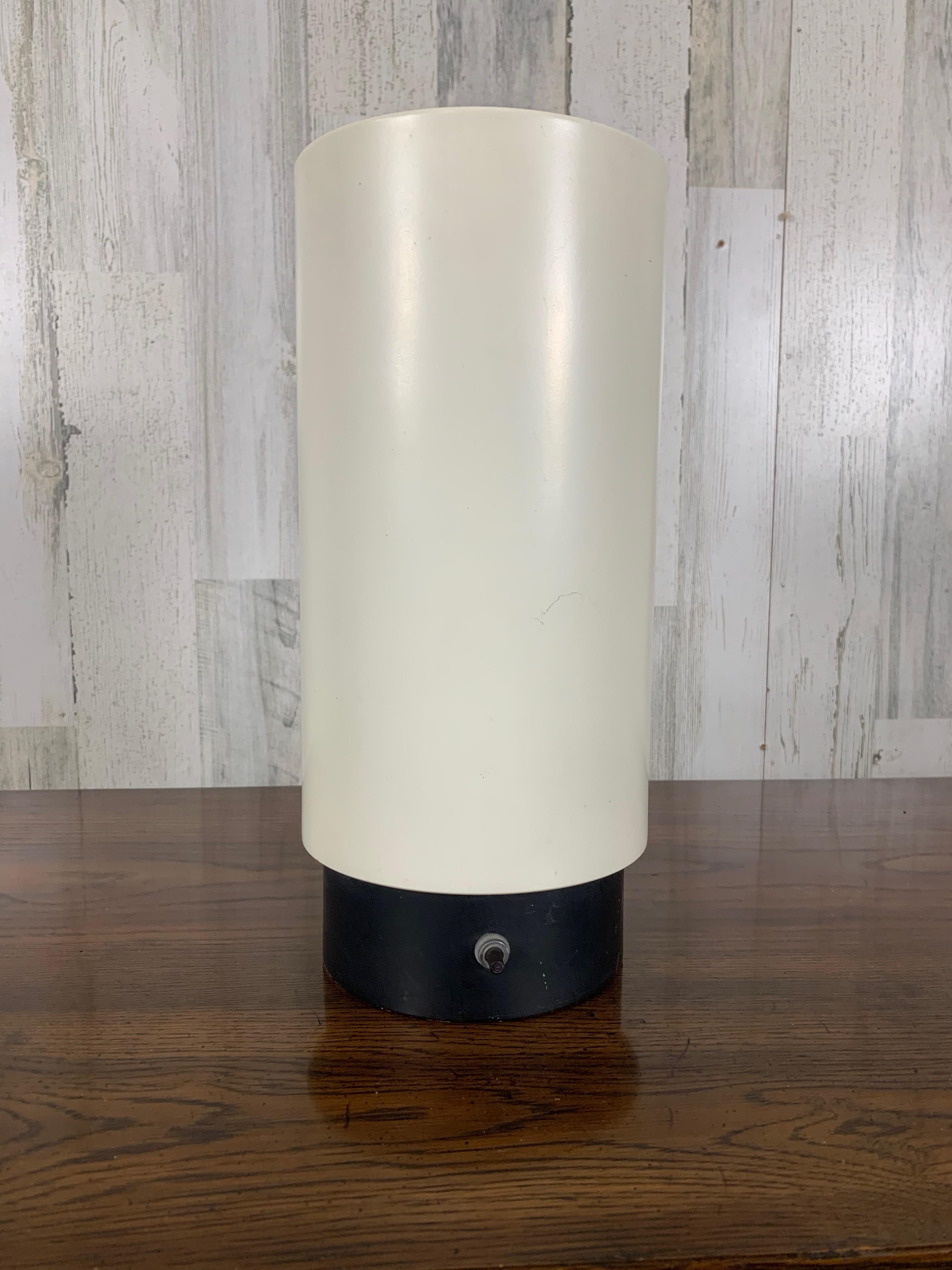 Aluminum cylinder with black metal base and pleated interior by Gerald Thurston. Best used as a floor up light to create a moody ambiance or to highlight a architechual element in the room.