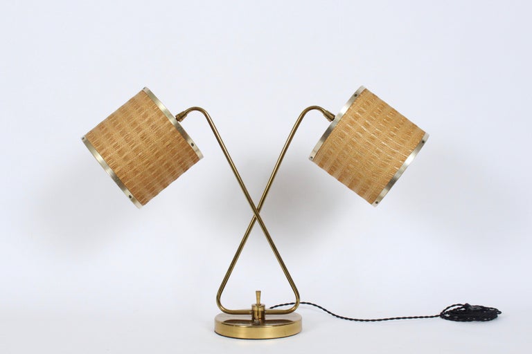 Gerald Thurston for Lightolier crossed swords desk lamp with brass rimmed Raffia Barrel Shades, 1950's. Featuring dual arms in Brass with adjusting, dual Brass rimmed, intertwined Raffia ribbon Shades on circular base. Original 7 H x 7 D Shades.