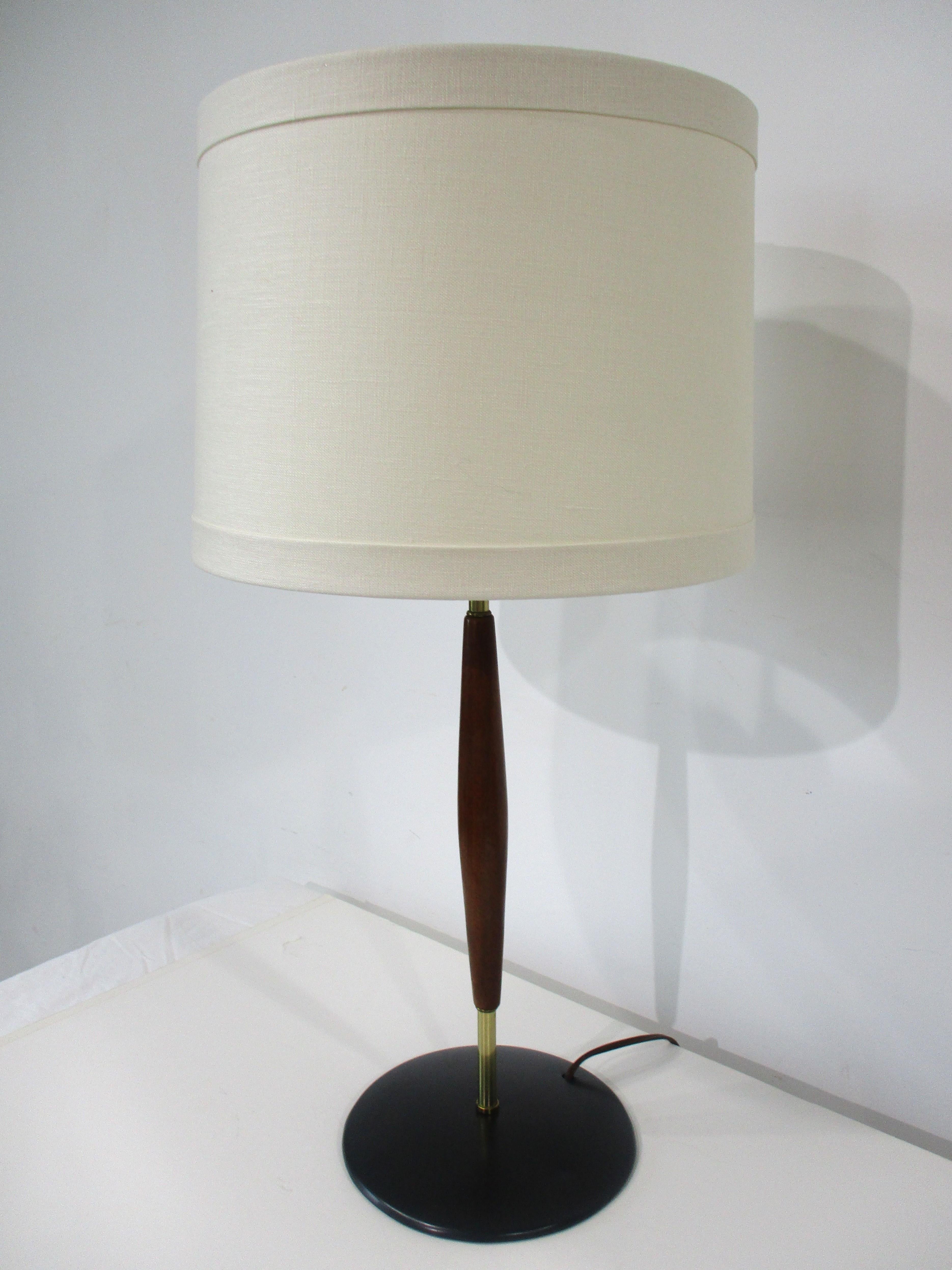 A very well tailored table lamp with black metal base , brass and walnut shaft  accented and topped with a oatmeal toned linen shade . A nice touch is the brushed brass final and the upper and lower bands to the shade making it a bit more dramatic