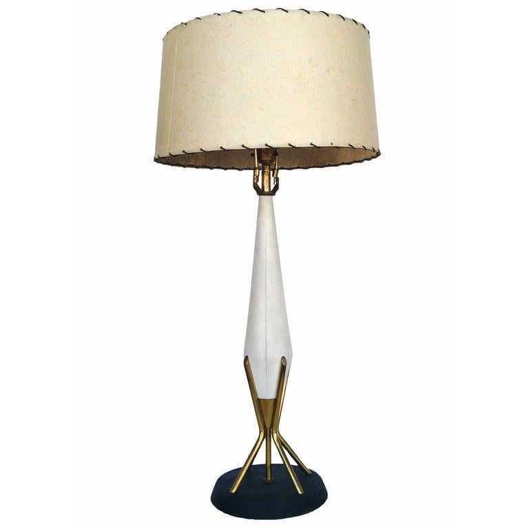 This Mid-century Thurston style table lamp has a modern elegance. The white painted sculptural wood center, bright brass accents, and atomic age fiberglass shade all meet to a black rounded base for a streamlined design serene only the 1950s could