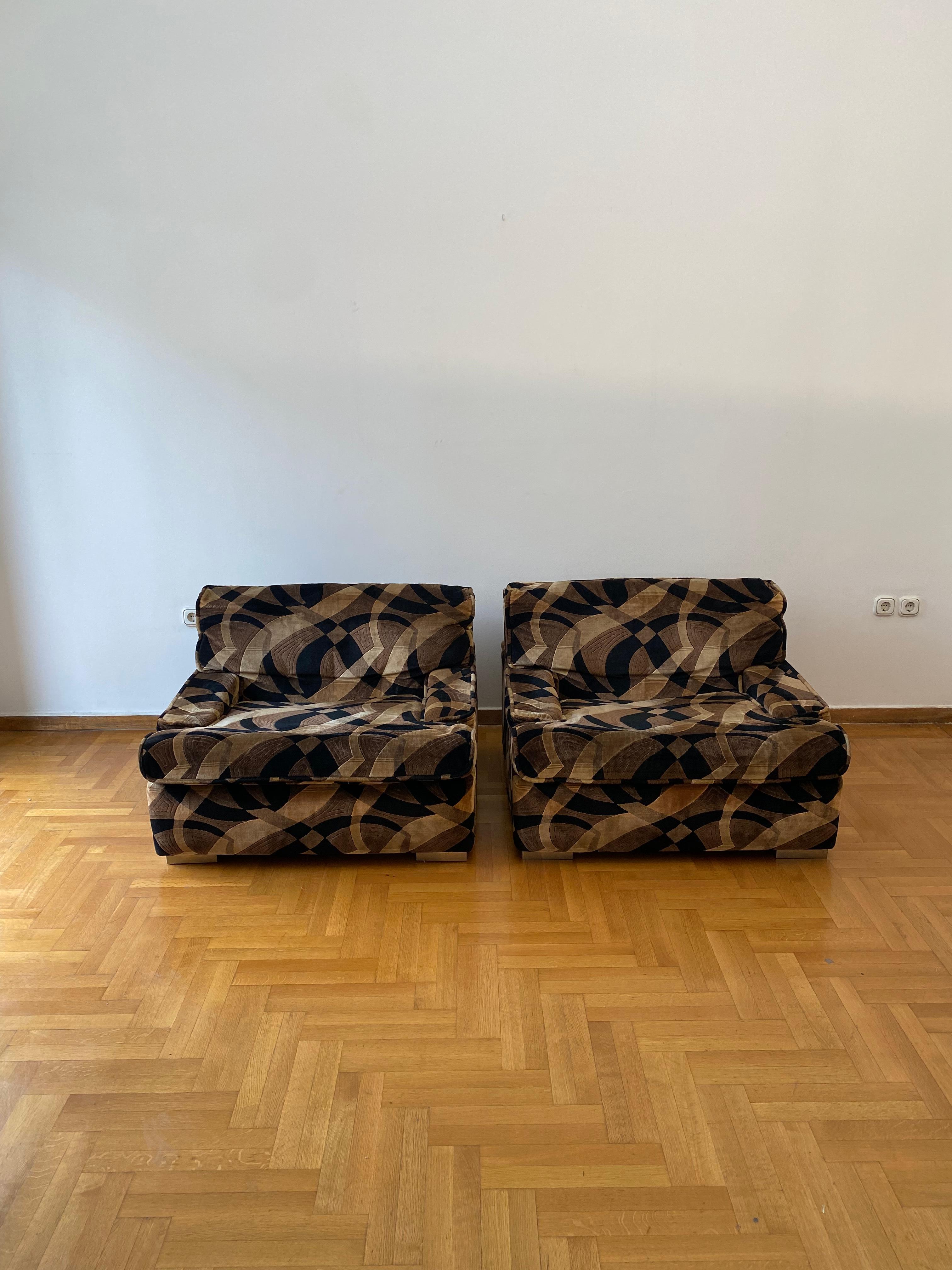 Si tratta di una splendida e rarissima coppia di poltrone di Gerard Guermonprez con il loro tessuto di velluto originale degli anni '70.

Hanno una sorta di forma a scatola con braccioli bassi e sedute comode, schienale curvo e piedini cromati.

Le