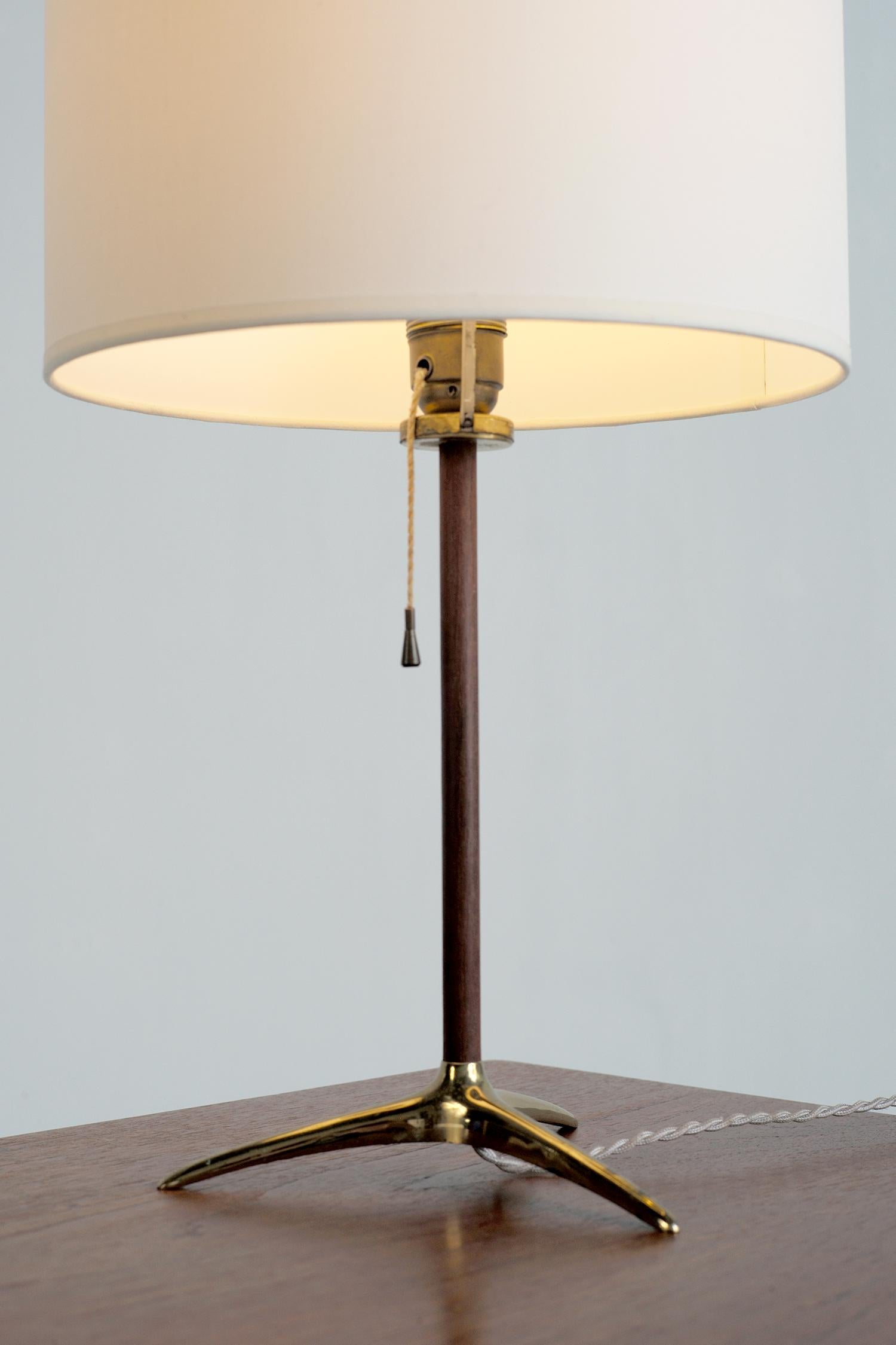 Elegante Tischleuchte von Gérard Thurston, USA 1950. Sie ruht auf einem dreibeinigen Sockel aus vergoldetem Messing, der Lauf ist aus Nussbaumholz. Die Zündung wird über einen Zugschalter betätigt. Der zylindrische Lampenschirm ist oben mit einer